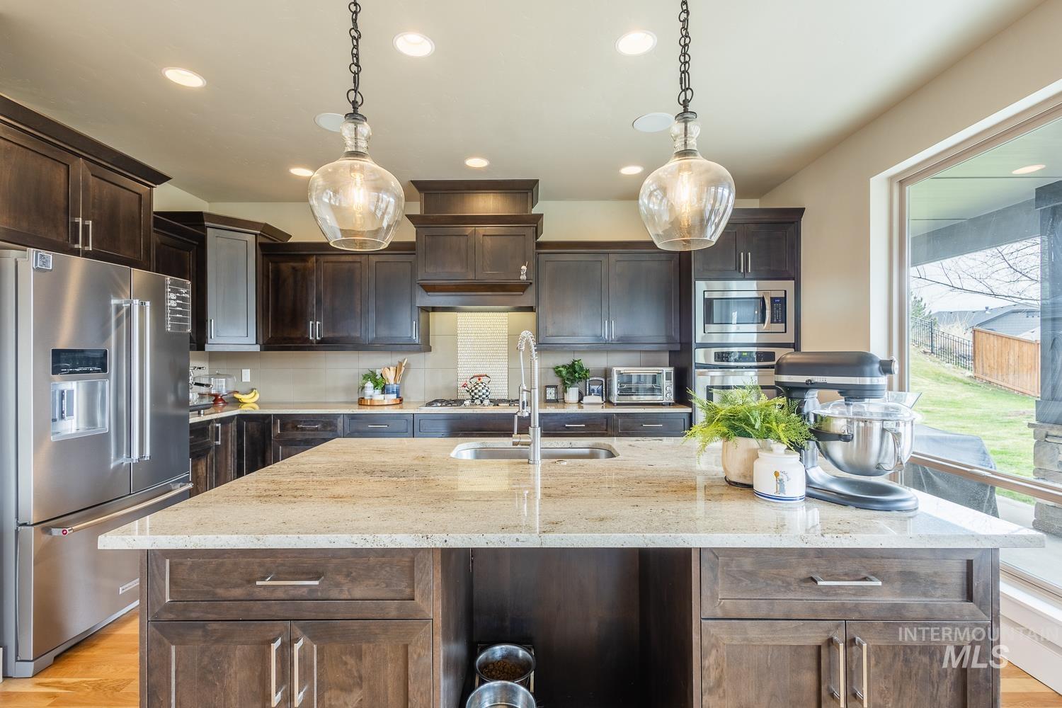 Kitchen with stainless steel appliances, light stone counters, dark wood finish cabinets, and decorative light fixtures