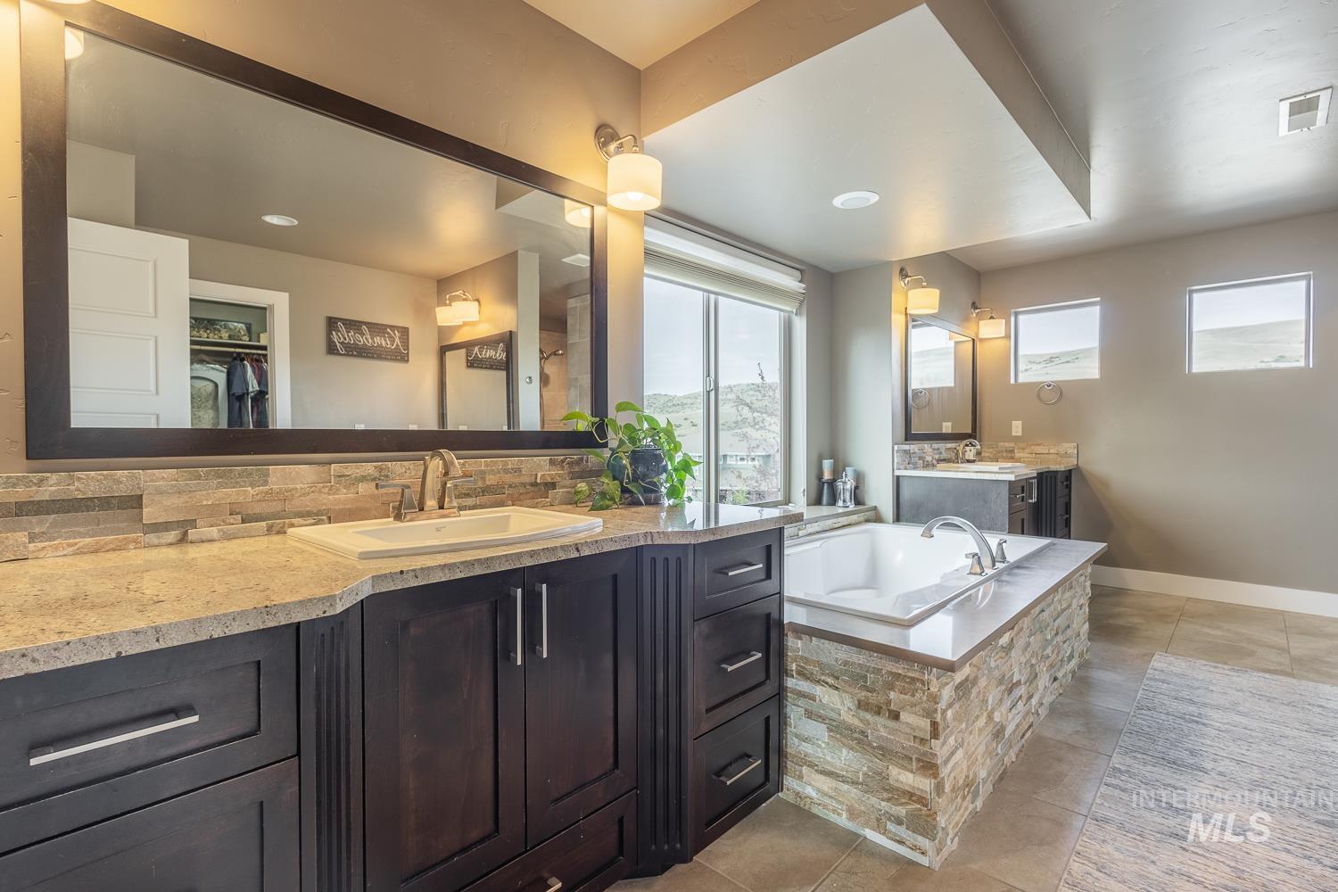 Bathroom featuring light tile patterned floors, two vanities, decorative backsplash, a bath, and a walk in closet