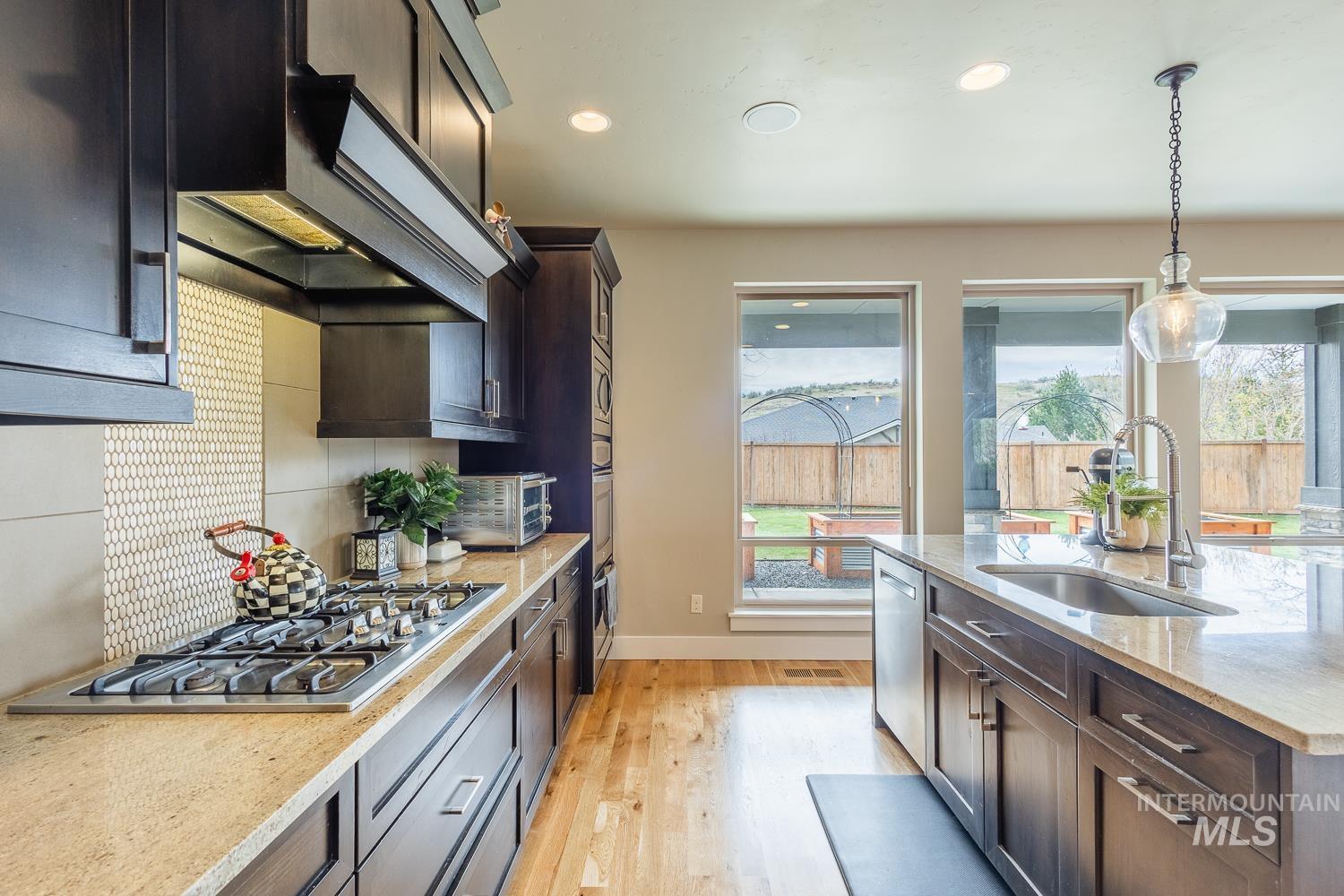 Kitchen featuring dark wood finish cabinets, light stone counters, stainless steel appliances, and extractor fan