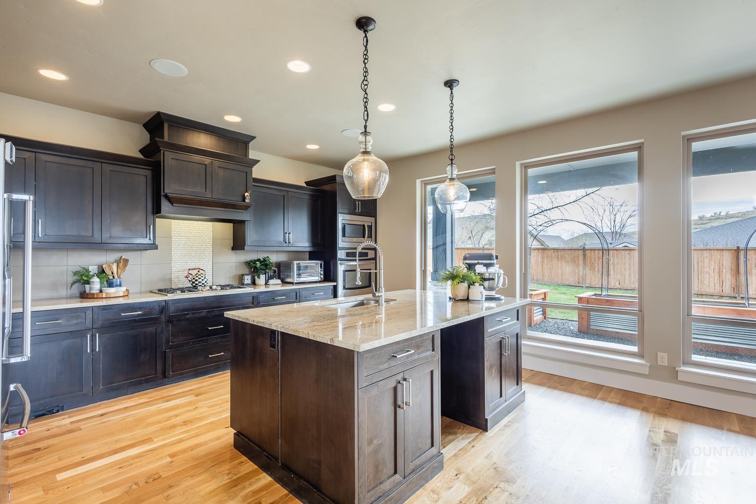 Kitchen featuring light stone counters, an island with sink, light wood-style floors, pendant lighting, and backsplash
