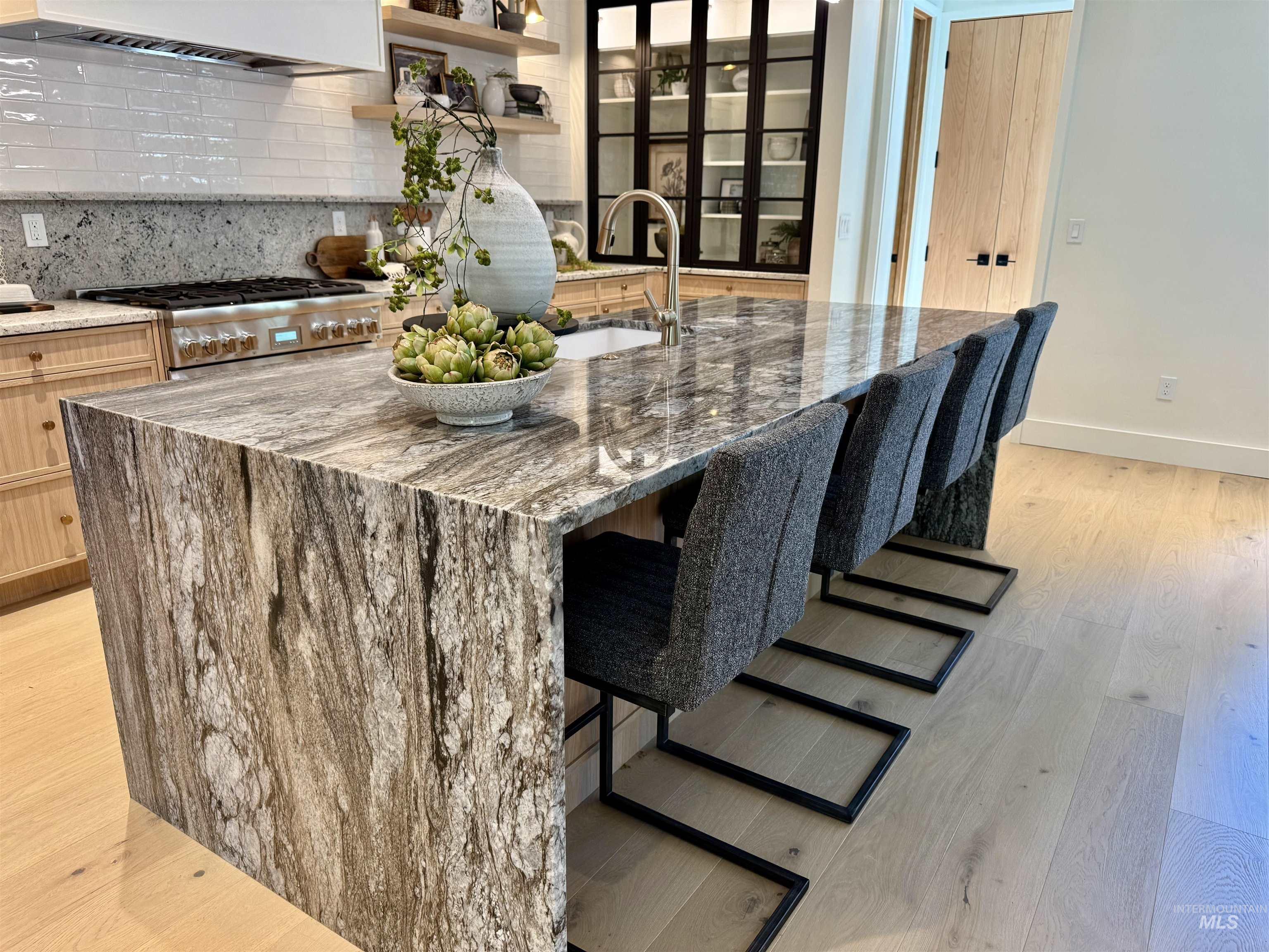 Kitchen featuring light stone countertops, tasteful backsplash, light wood-style floors, a kitchen breakfast bar, and an island with sink