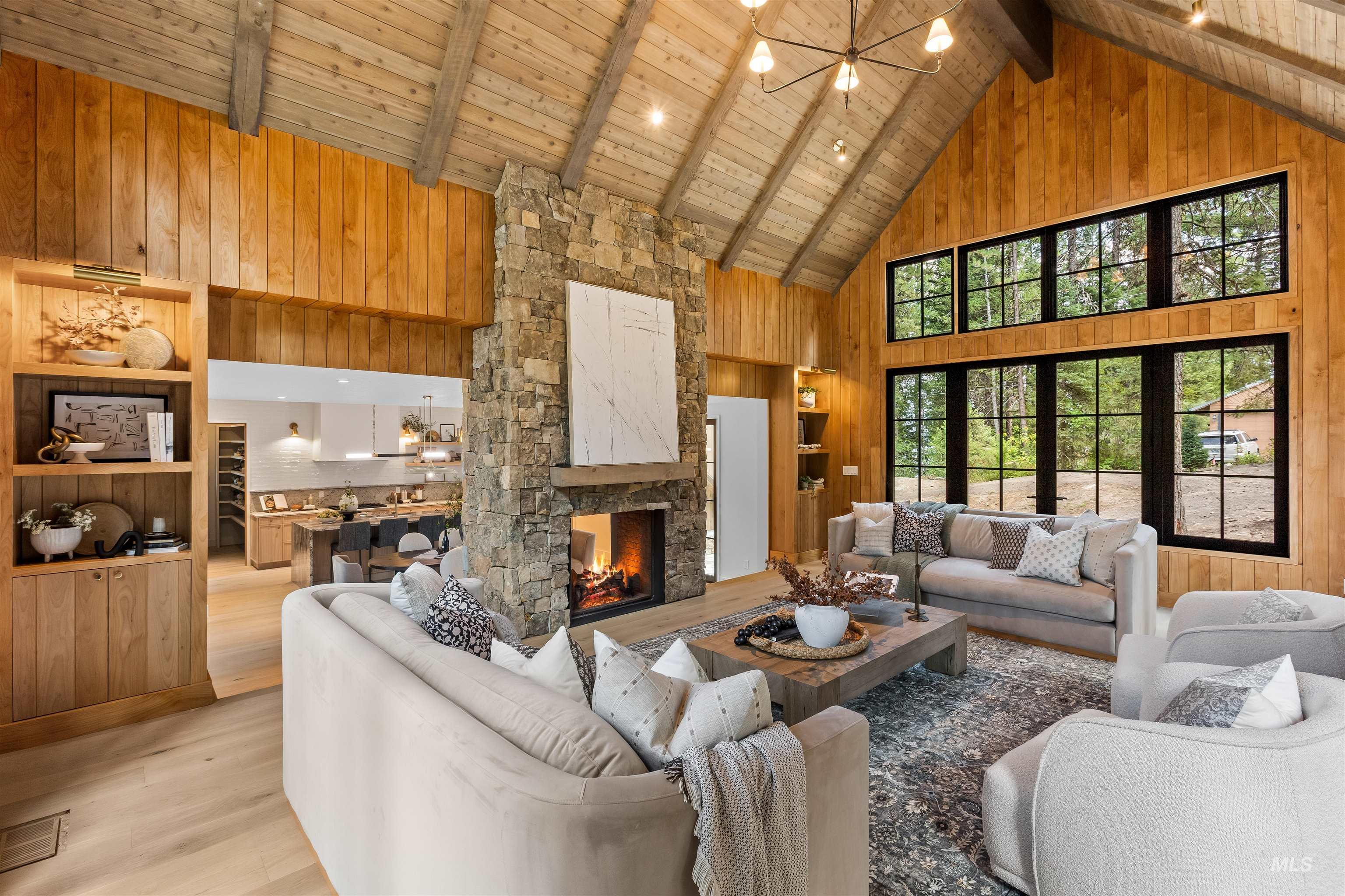 Living room with wooden walls, high vaulted ceiling, a chandelier, a stone fireplace, and a wooden ceiling with exposed beams