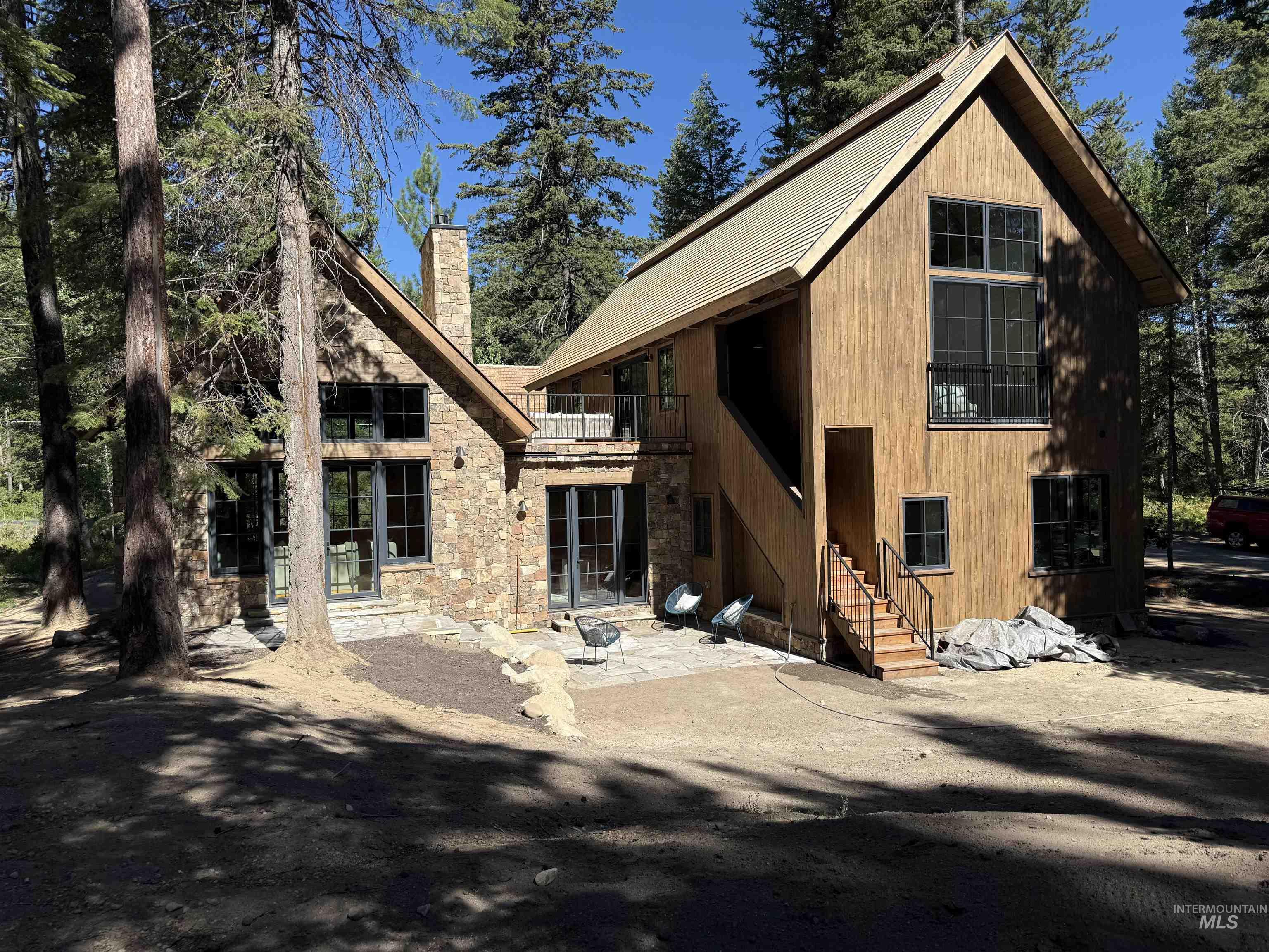 View of front of house with a patio, a chimney, stone siding, and a balcony