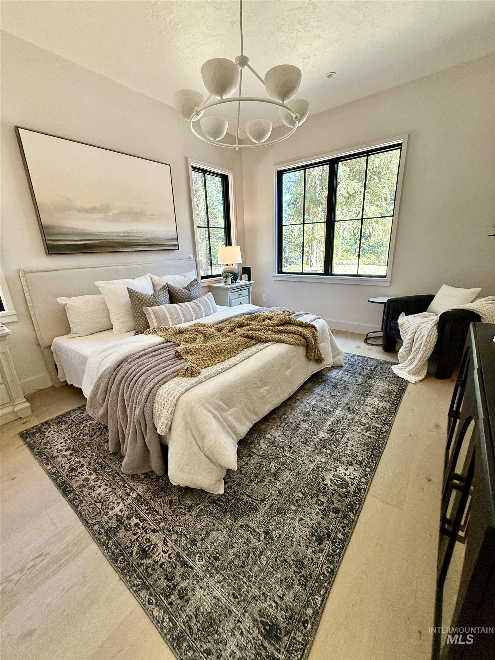 Bedroom featuring a textured ceiling, multiple windows, light wood-style flooring, and a chandelier