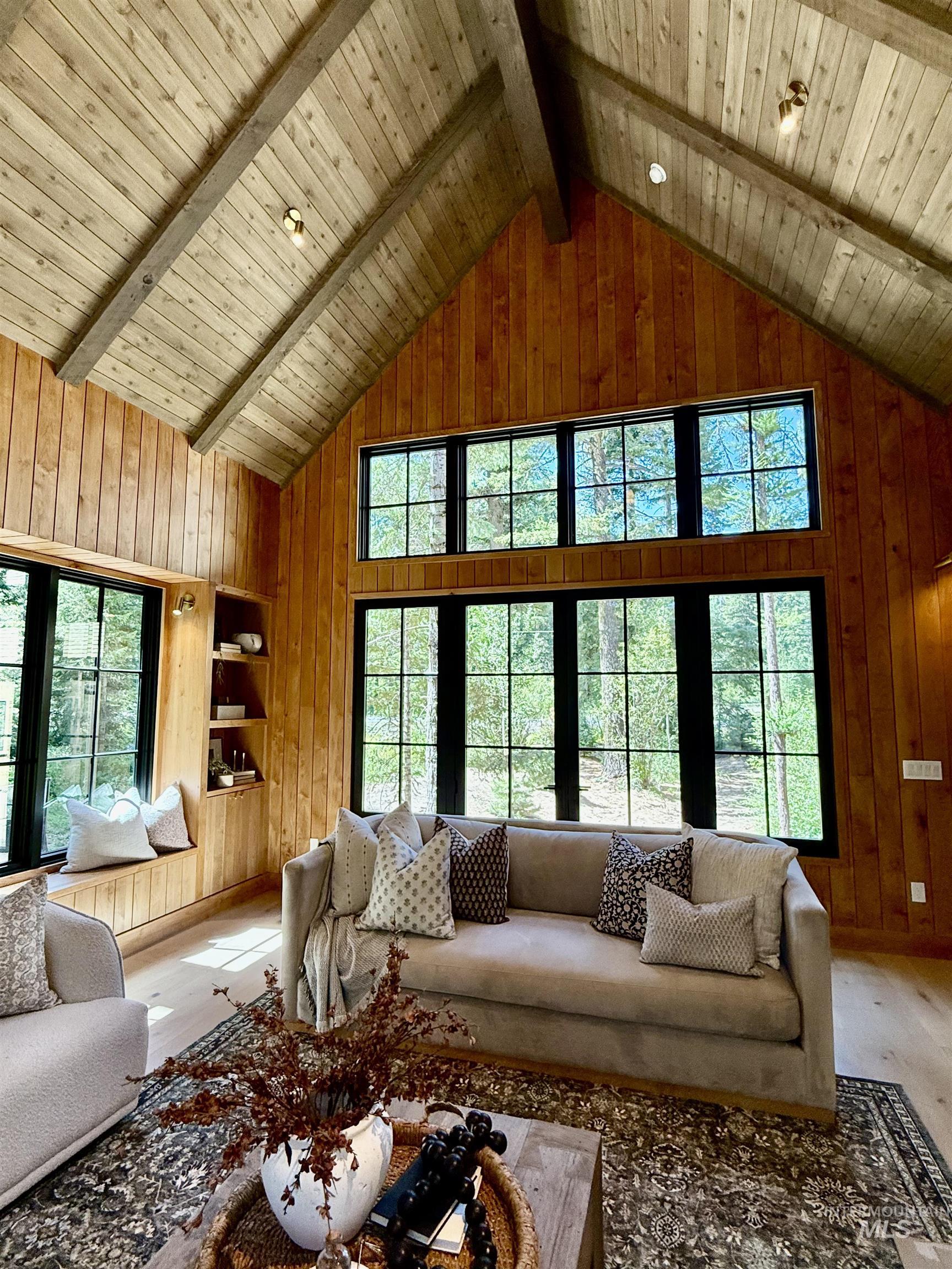 Living area featuring wood walls, high vaulted ceiling, and a wooden ceiling with exposed beams