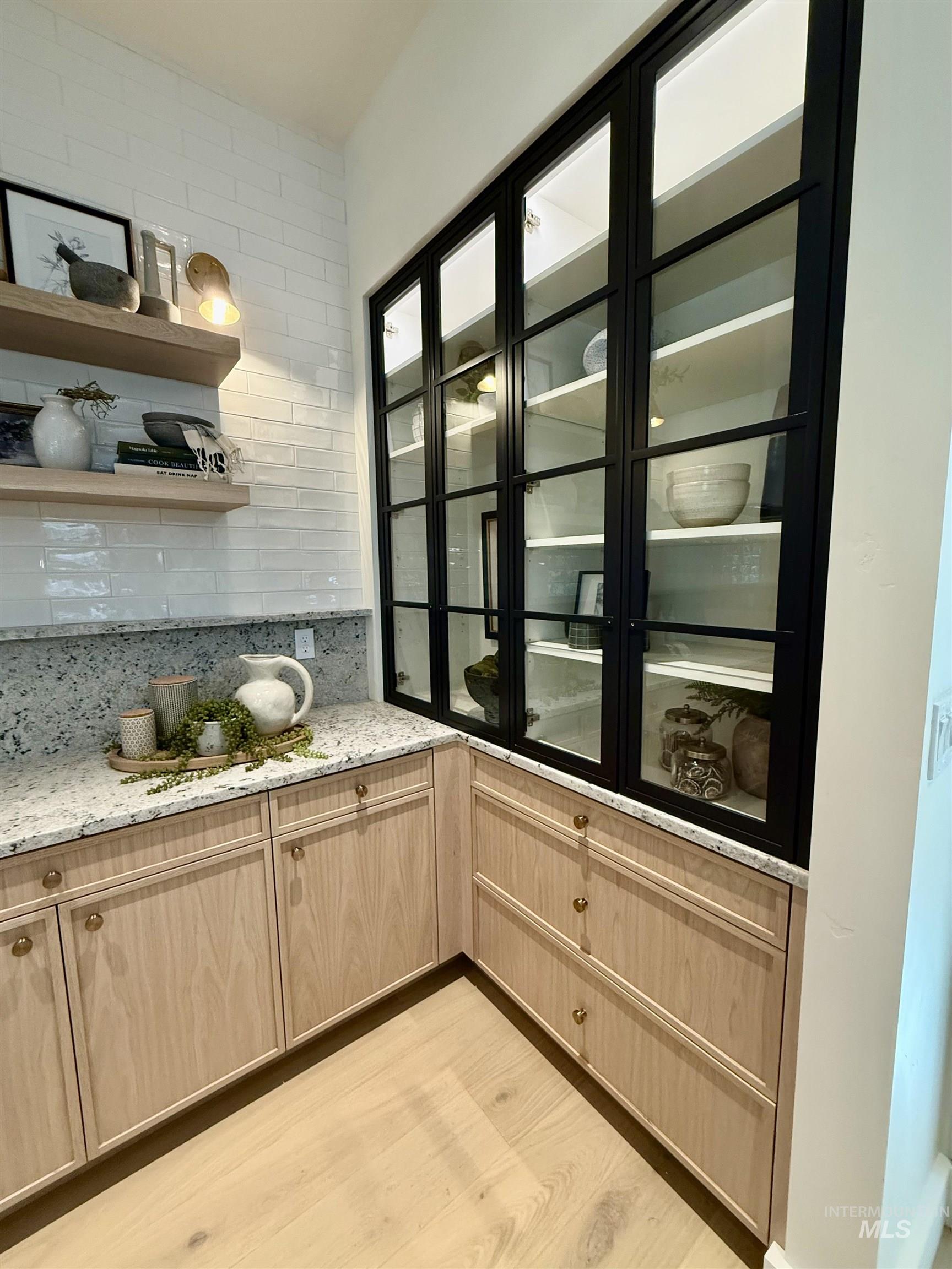 Bar area featuring light brown cabinets, light stone countertops, decorative backsplash, and light wood-style floors