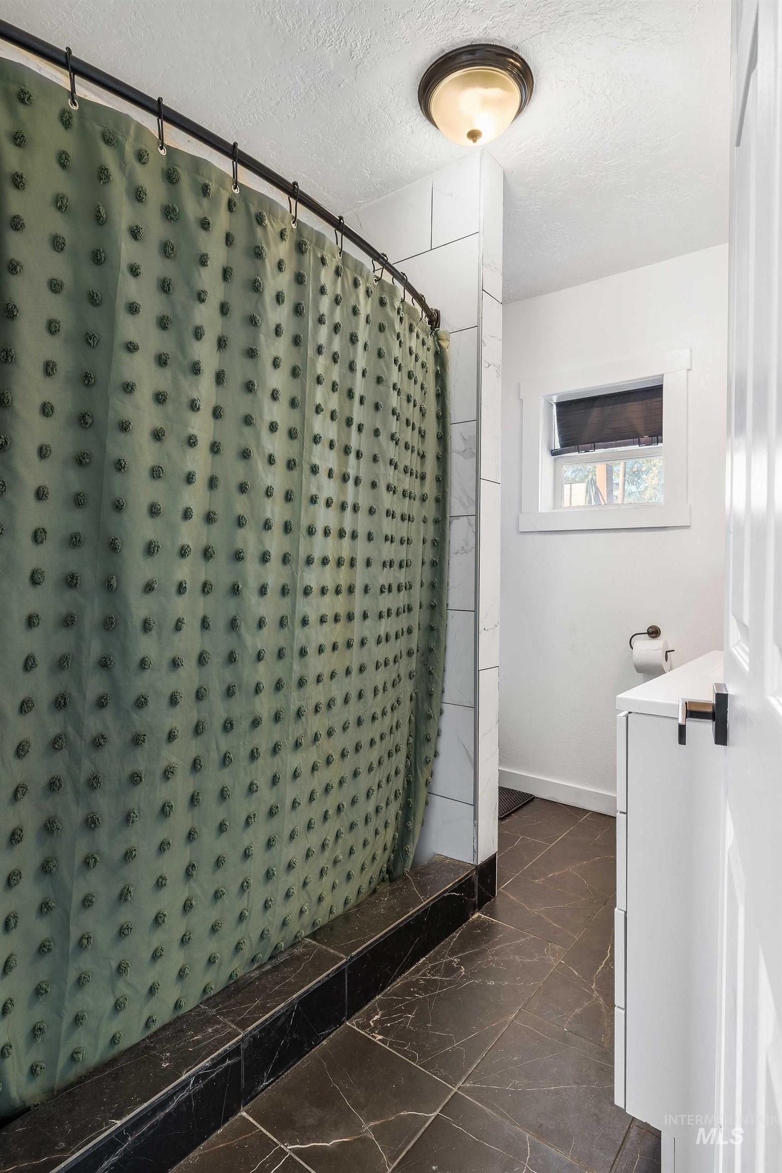 Bathroom featuring dark marble finish floors, a textured ceiling, a stall shower, and vanity