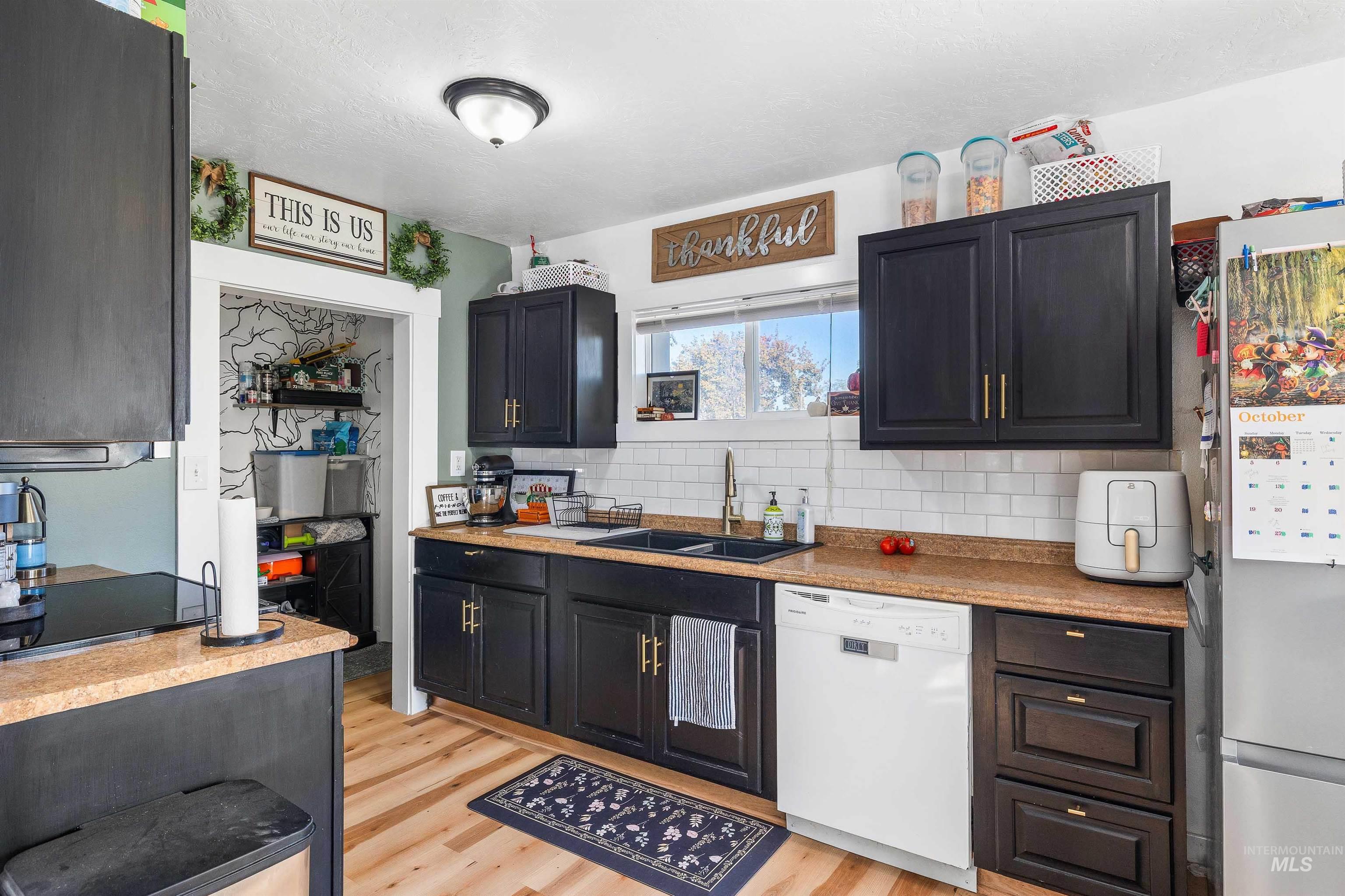 Kitchen featuring white dishwasher, light wood finished floors, freestanding refrigerator, and light countertops