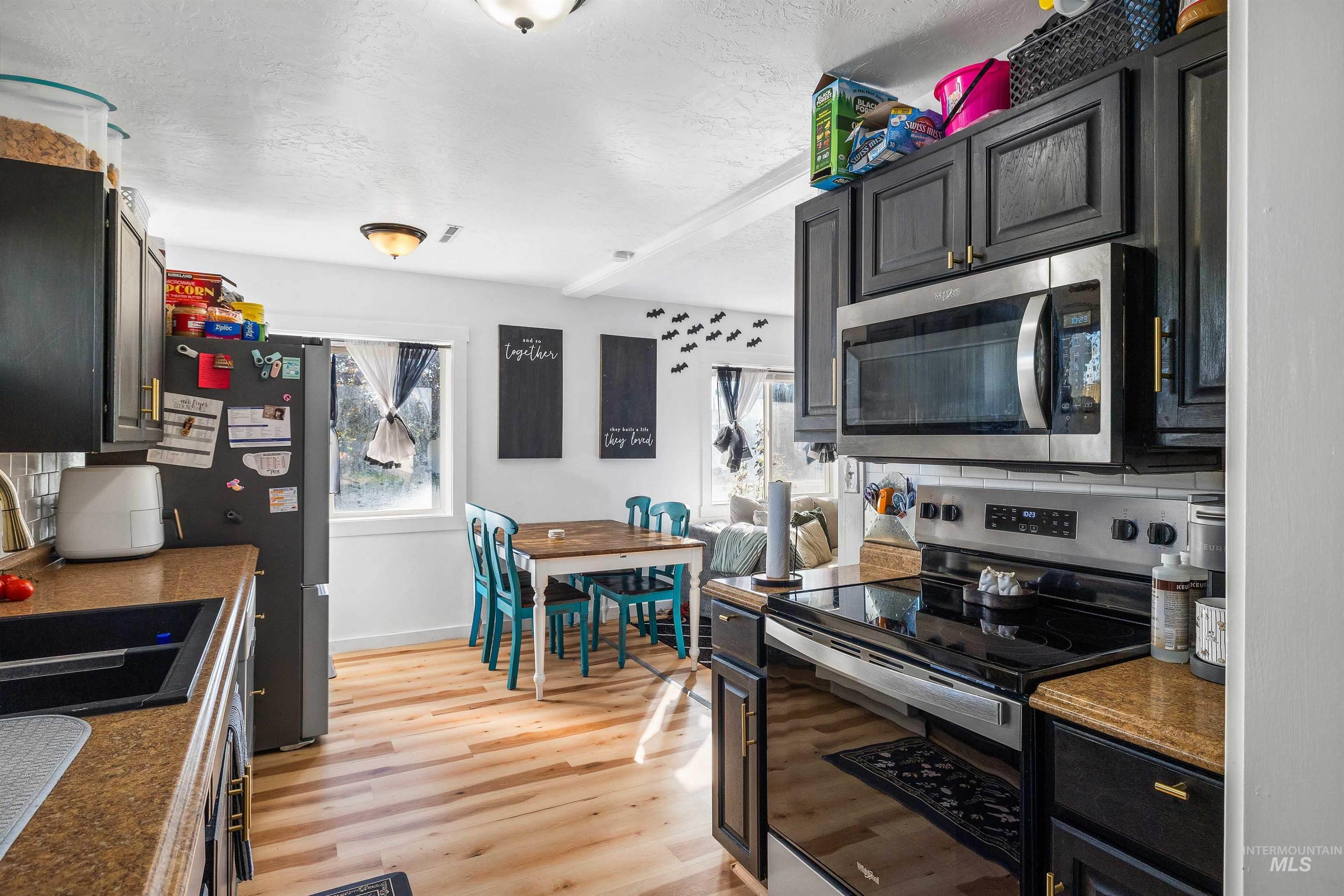 Kitchen with appliances with stainless steel finishes, tasteful backsplash, light wood-style flooring, a textured ceiling, and dark cabinetry
