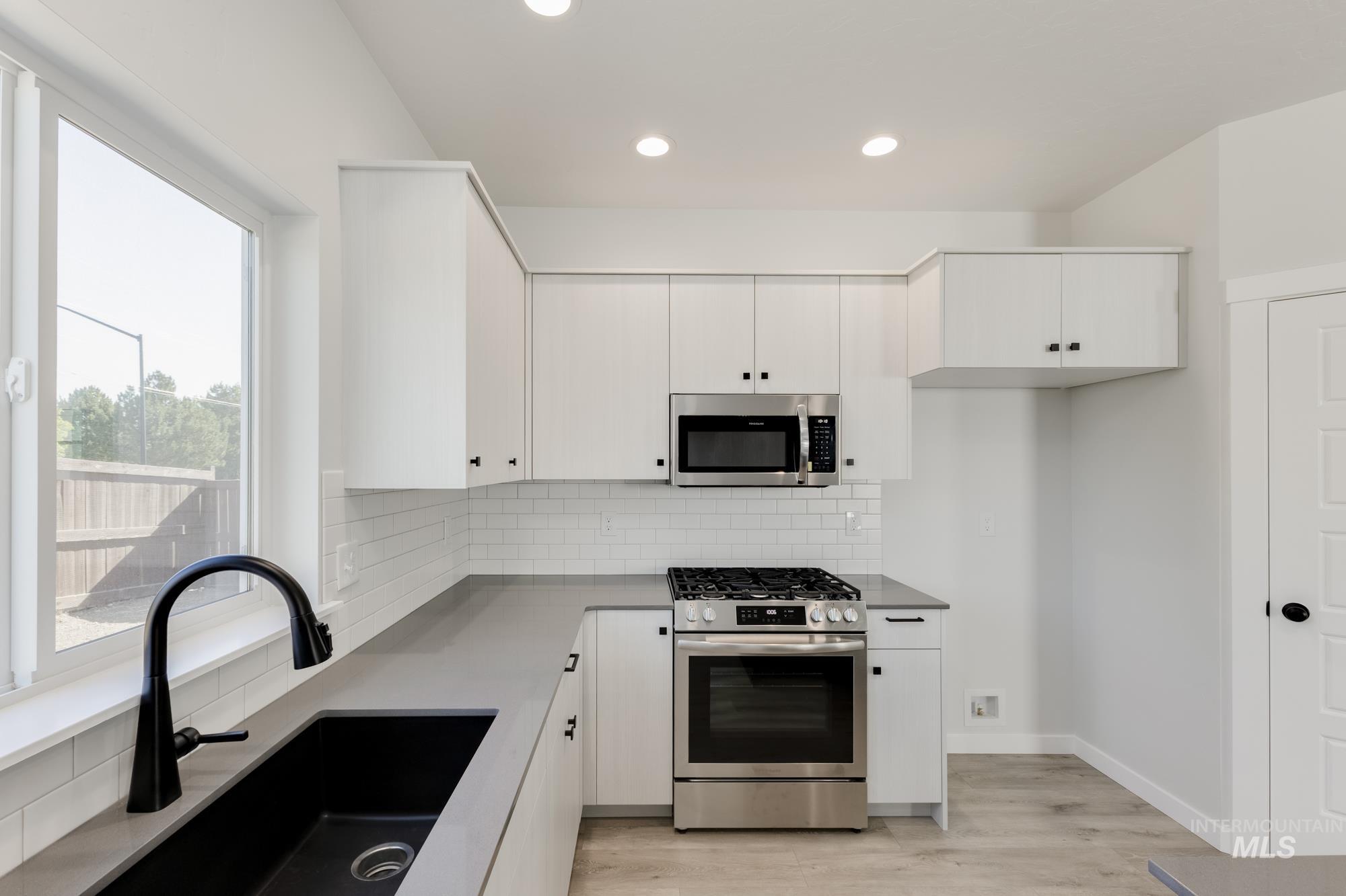 Kitchen featuring appliances with stainless steel finishes, white cabinetry, backsplash, and recessed lighting