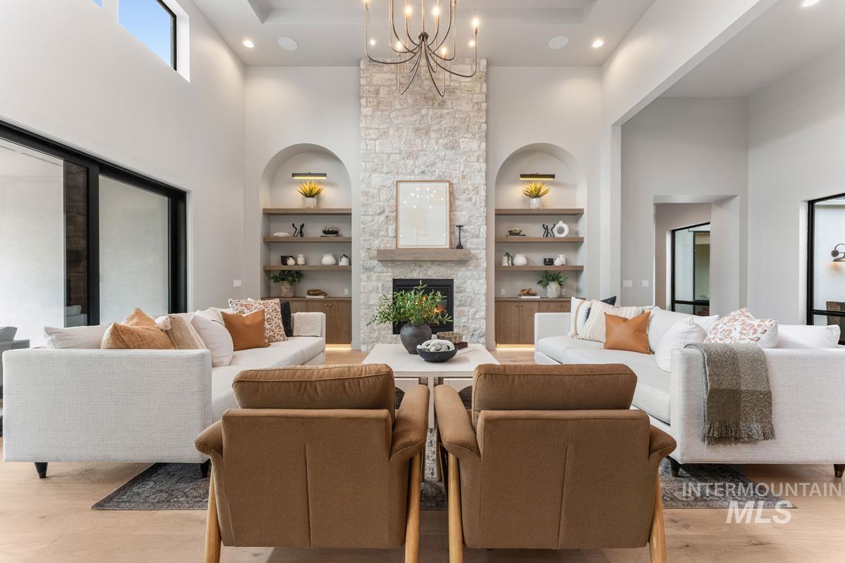 Living room featuring suspended lighting, a high ceiling, a fireplace, light wood-style flooring, and built in features
