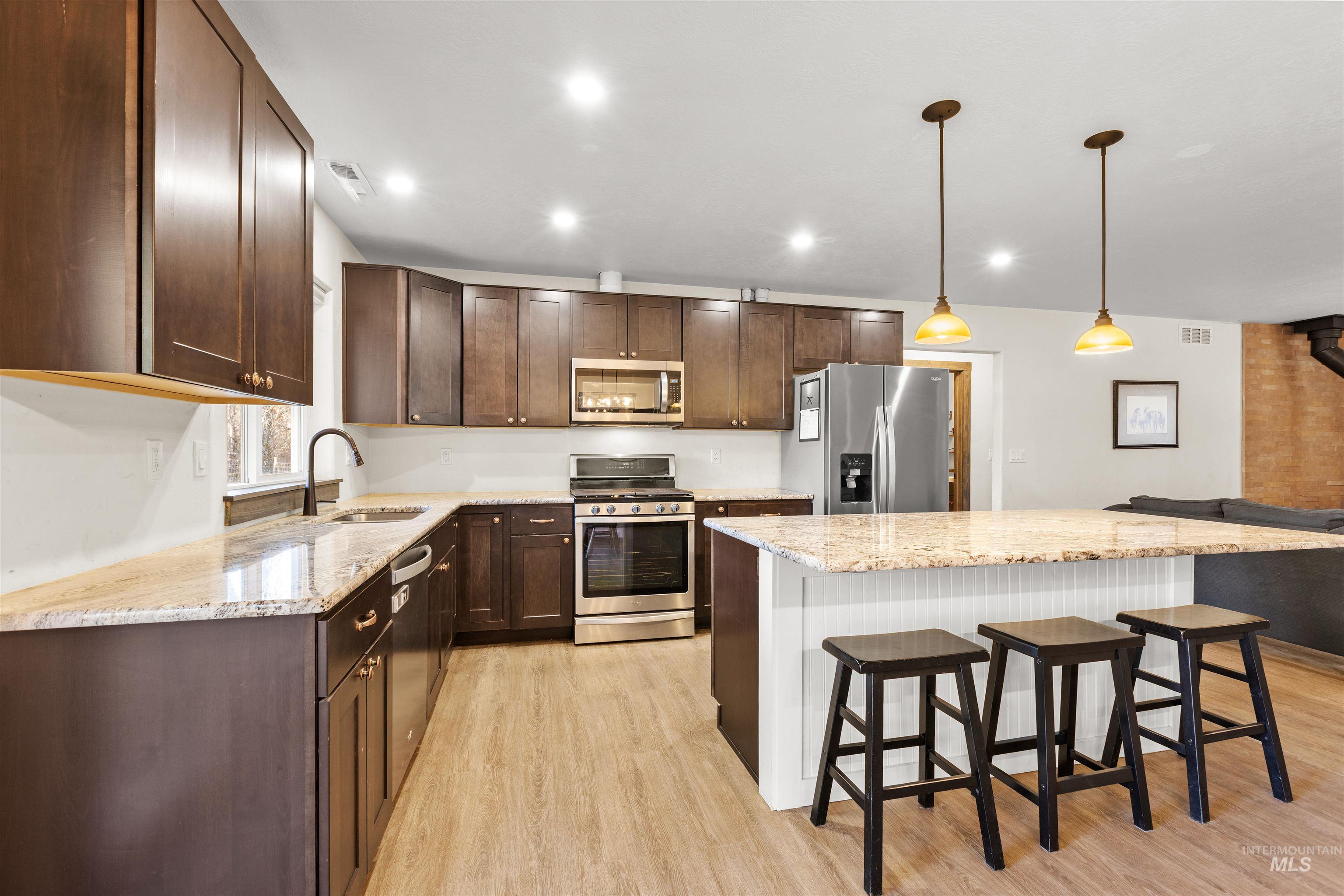 Kitchen featuring appliances with stainless steel finishes, light stone countertops, dark brown cabinets, a kitchen breakfast bar, and recessed lighting