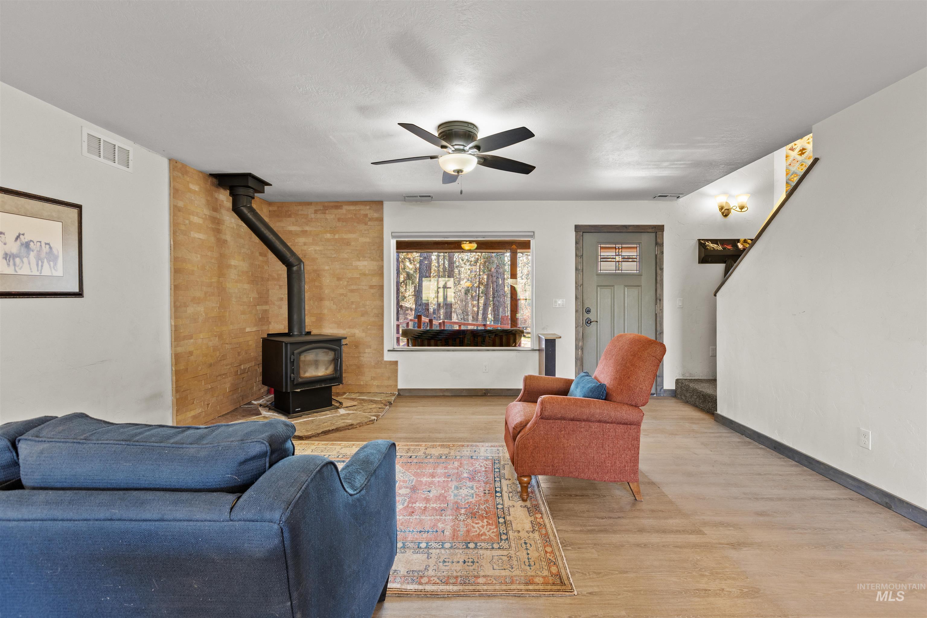 Living room with a wood stove, wood finished floors, a ceiling fan, and stairway