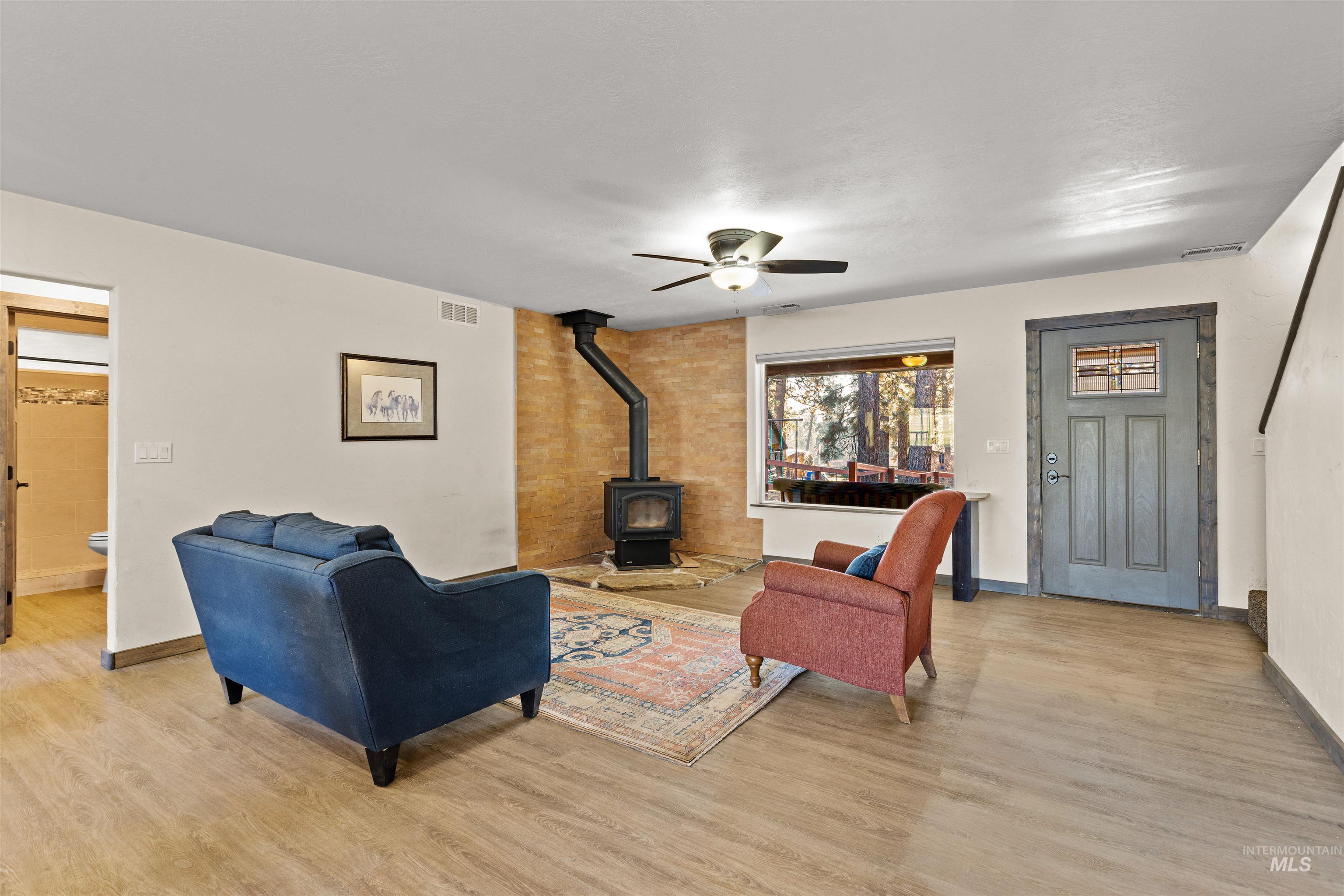 Living area featuring a wood stove, light wood-style flooring, and ceiling fan