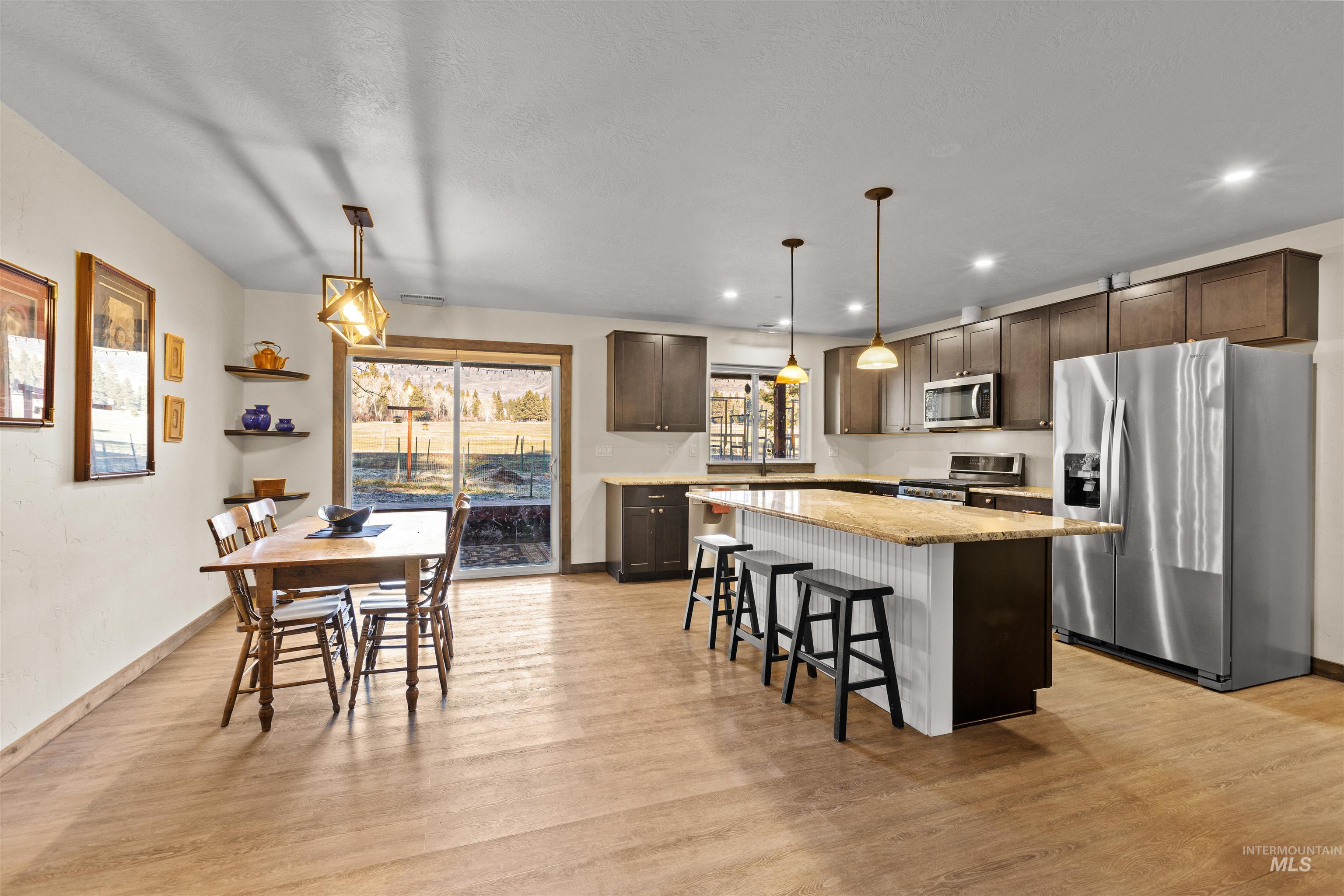 Kitchen with appliances with stainless steel finishes, dark brown cabinetry, a breakfast bar, decorative light fixtures, and a kitchen island