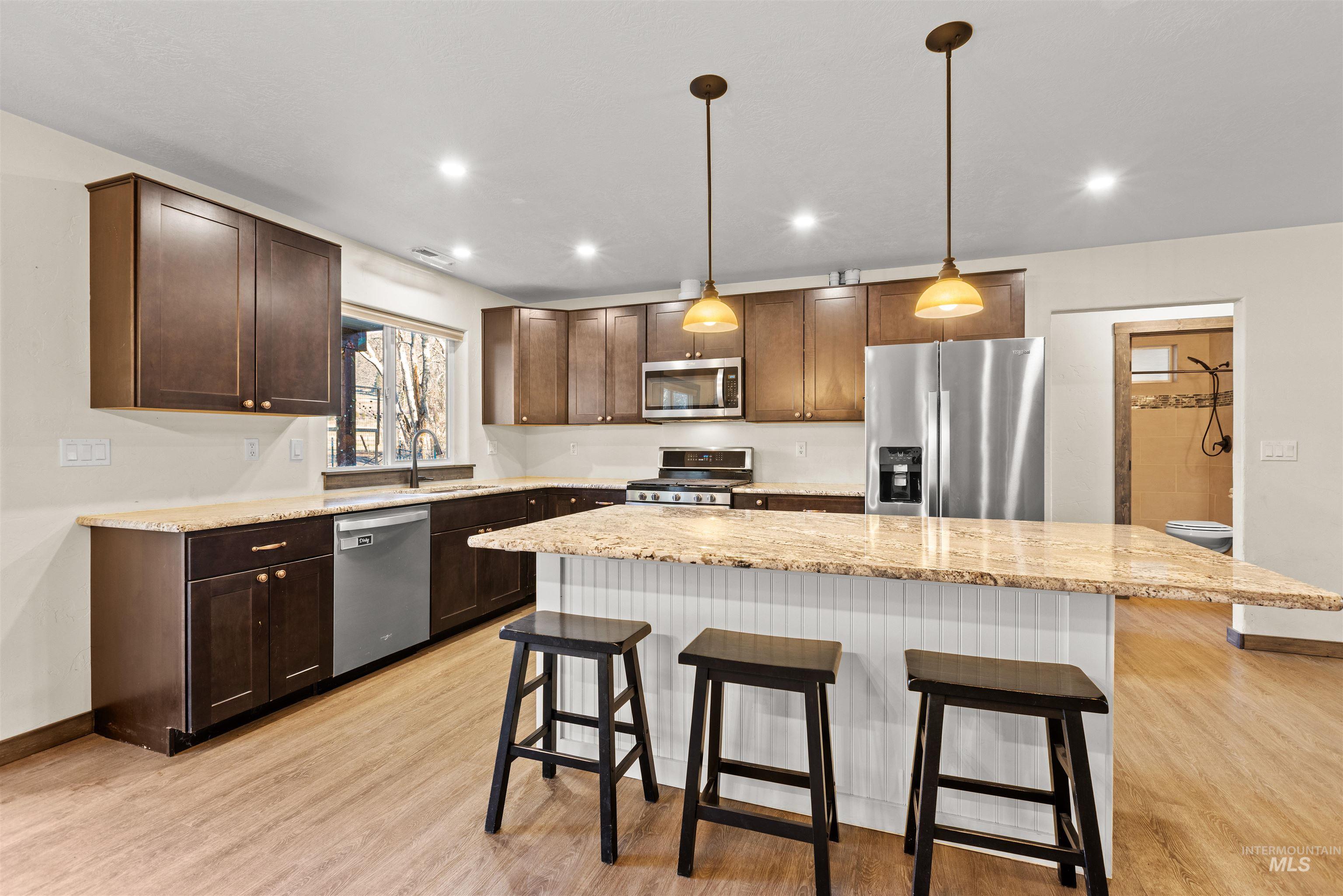 Kitchen with a breakfast bar area, appliances with stainless steel finishes, pendant lighting, light stone countertops, and a center island
