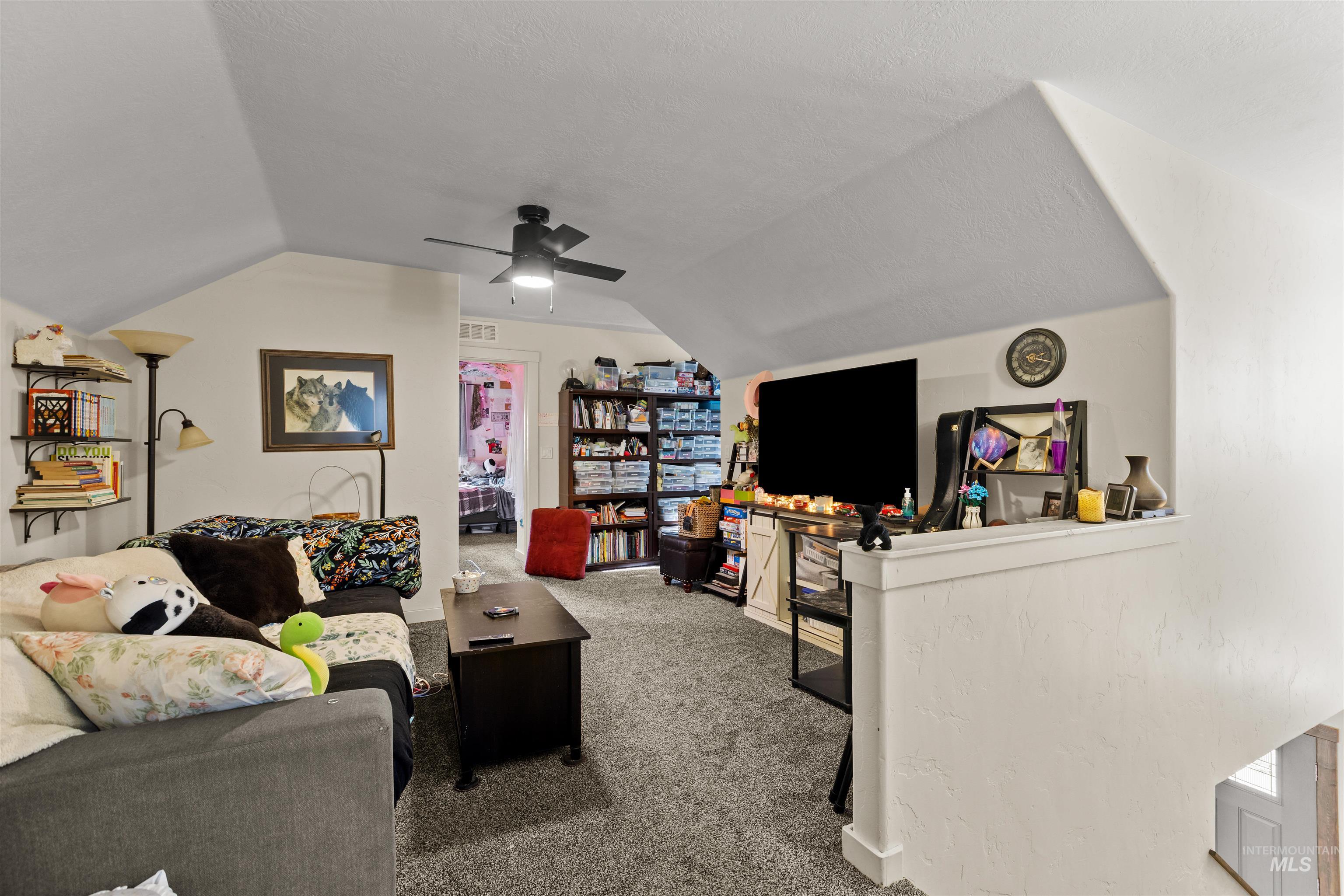 Carpeted landing area featuring vaulted ceiling, a ceiling fan, and a textured ceiling