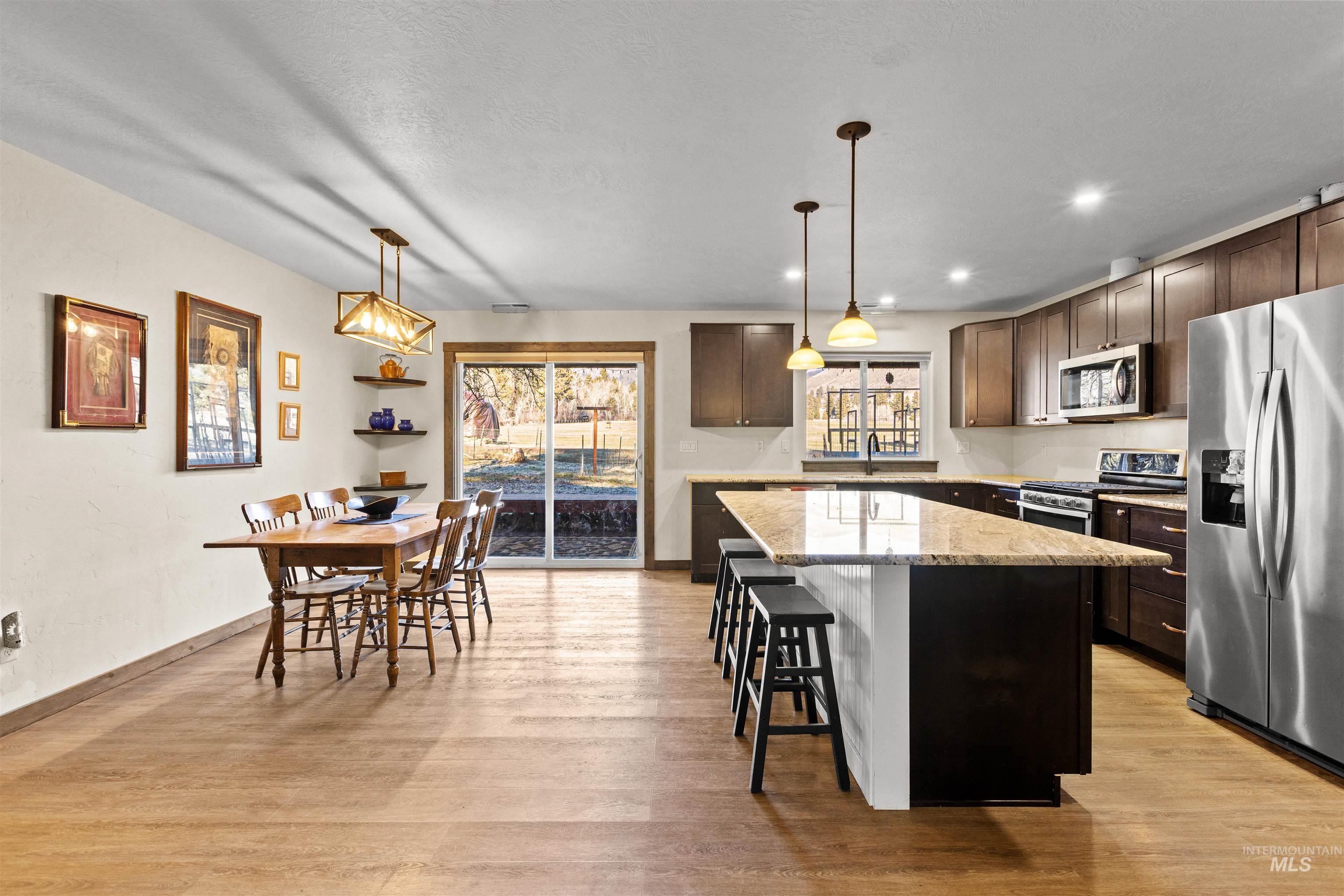 Kitchen featuring decorative light fixtures, appliances with stainless steel finishes, light stone counters, a center island, and a breakfast bar area