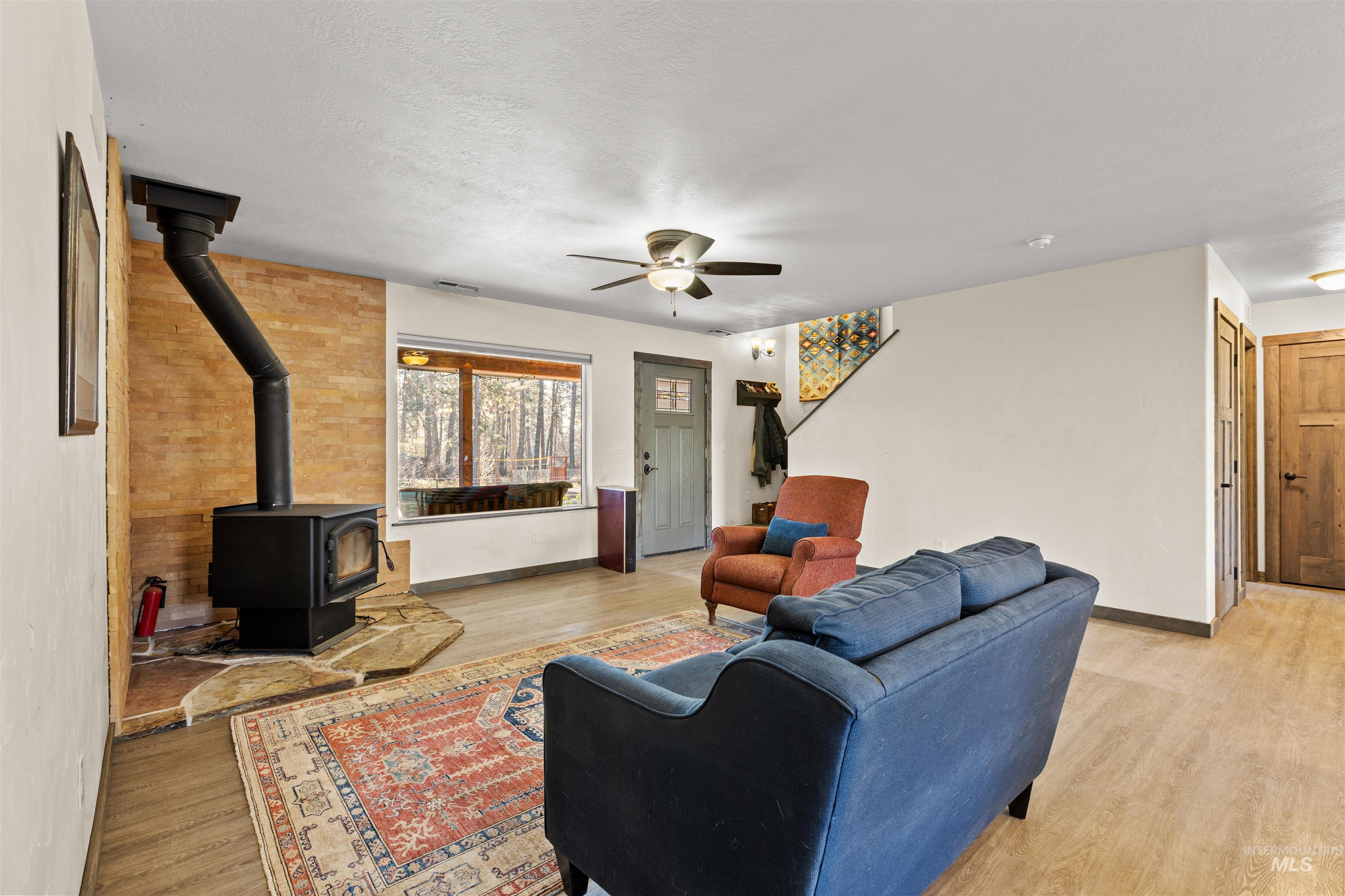 Living room with a wood stove, light wood-style flooring, and a ceiling fan