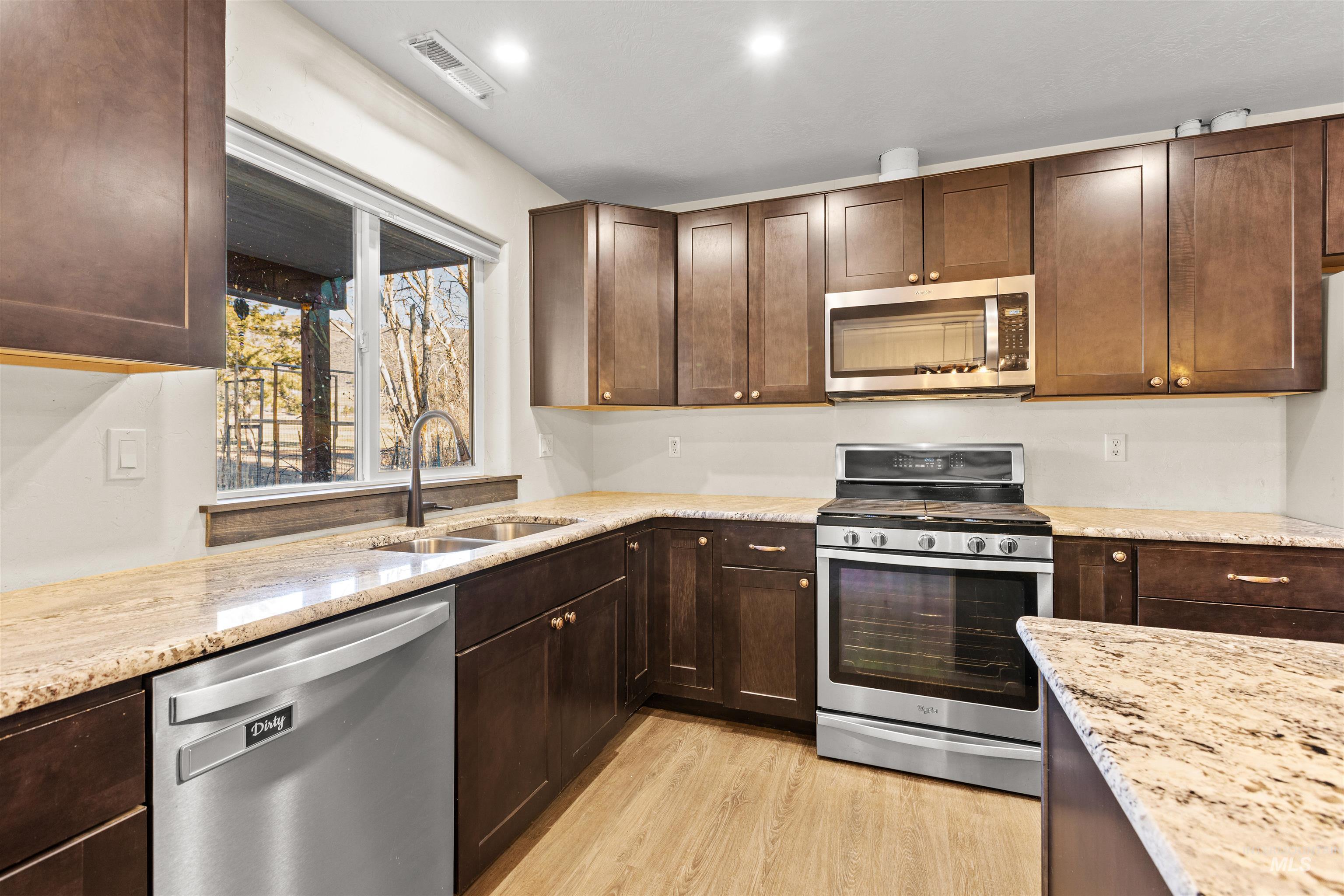 Kitchen with appliances with stainless steel finishes, dark brown cabinetry, and light stone counters
