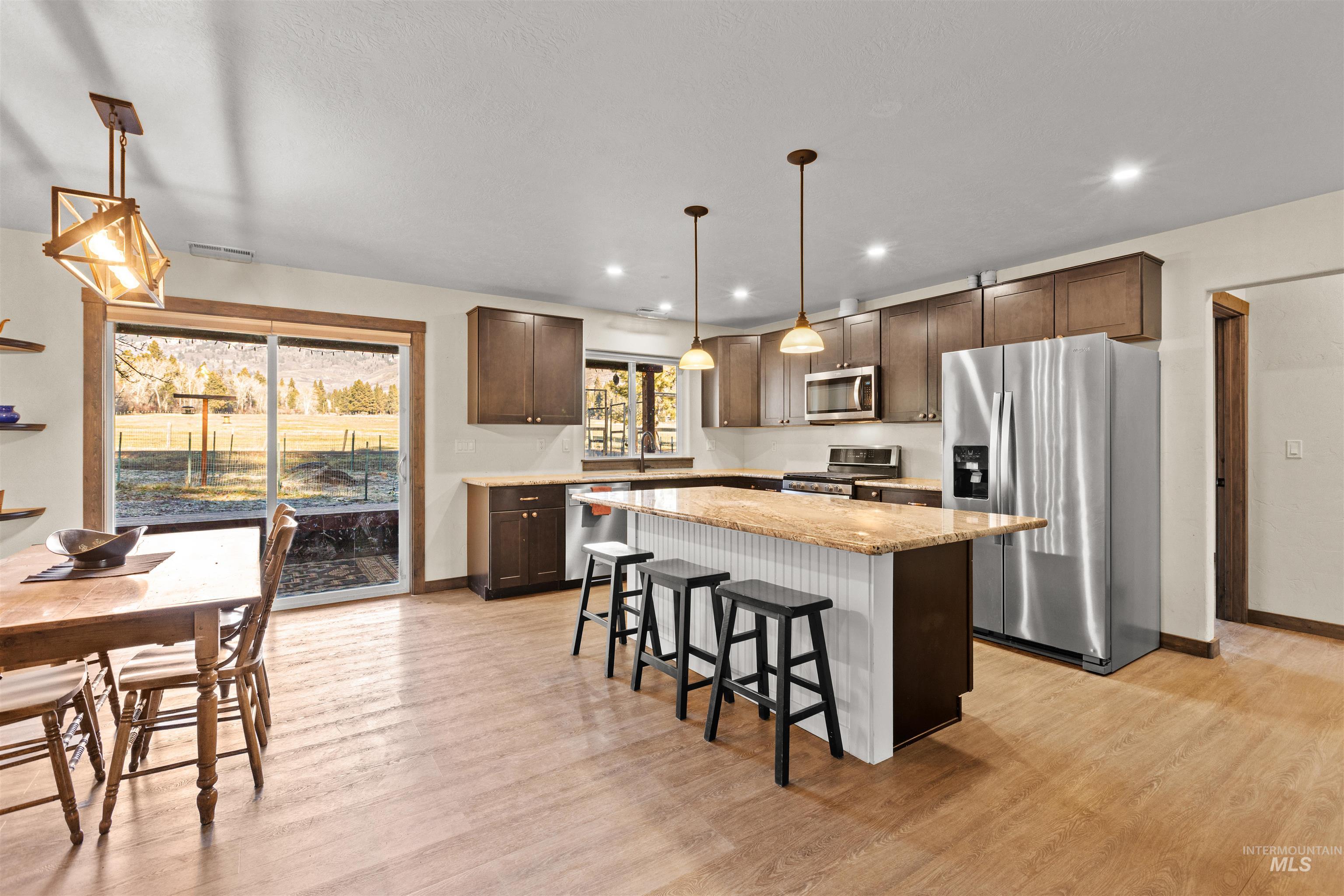 Kitchen featuring appliances with stainless steel finishes, a breakfast bar, dark brown cabinetry, a center island, and light stone counters