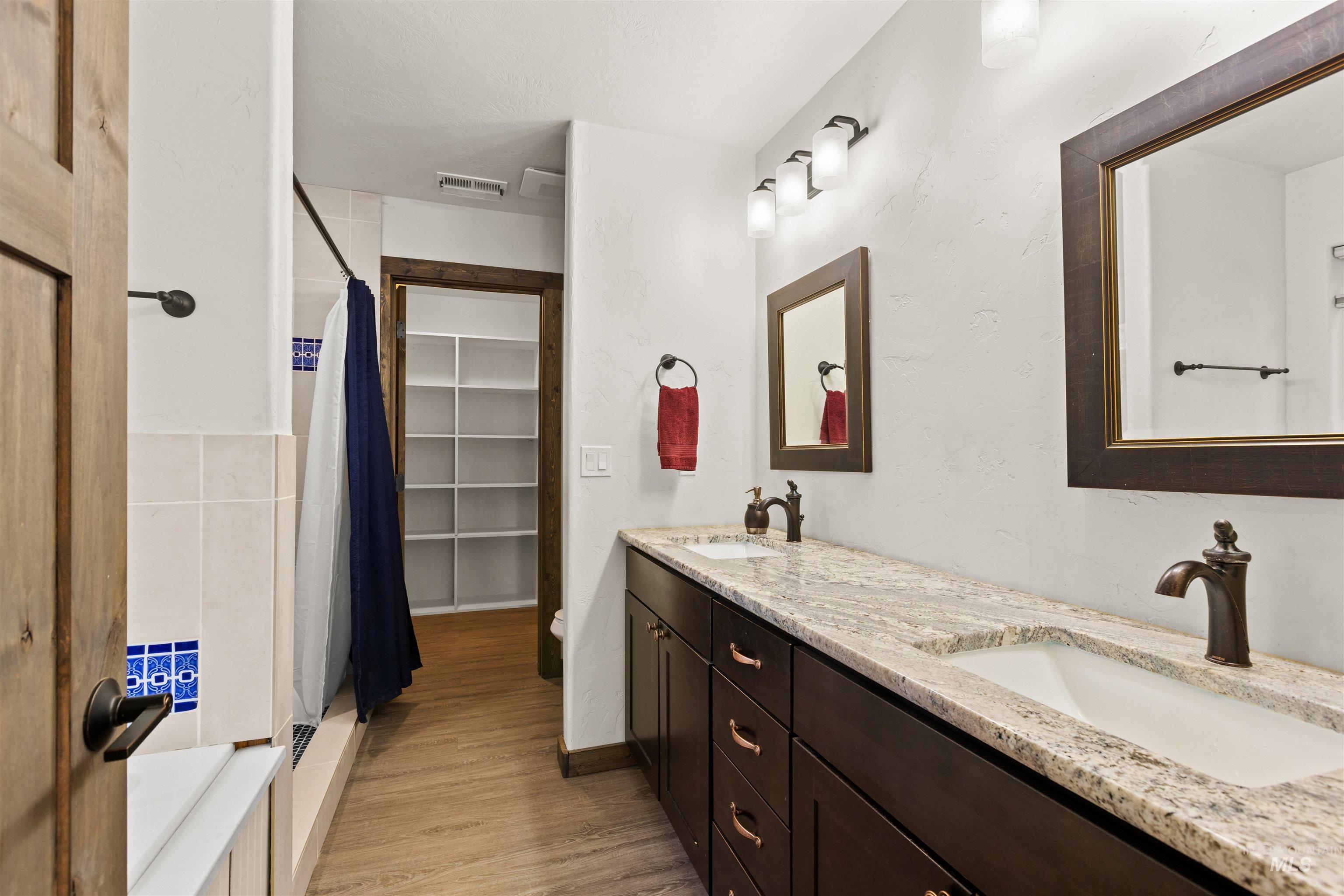 Bathroom with a shower stall, double vanity, light wood finished floors, and a walk in closet
