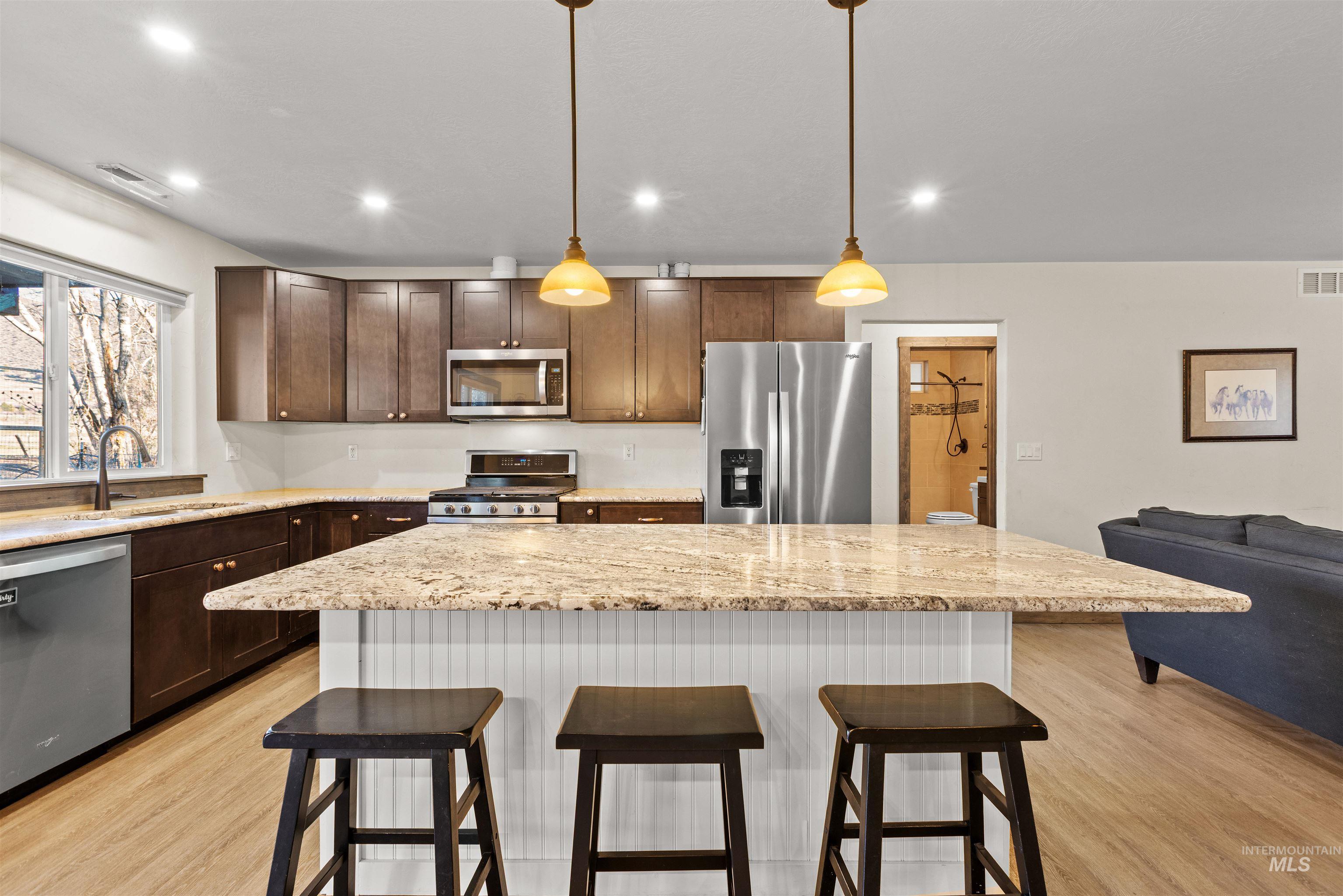 Kitchen featuring a kitchen bar, a center island, light stone countertops, stainless steel appliances, and hanging light fixtures