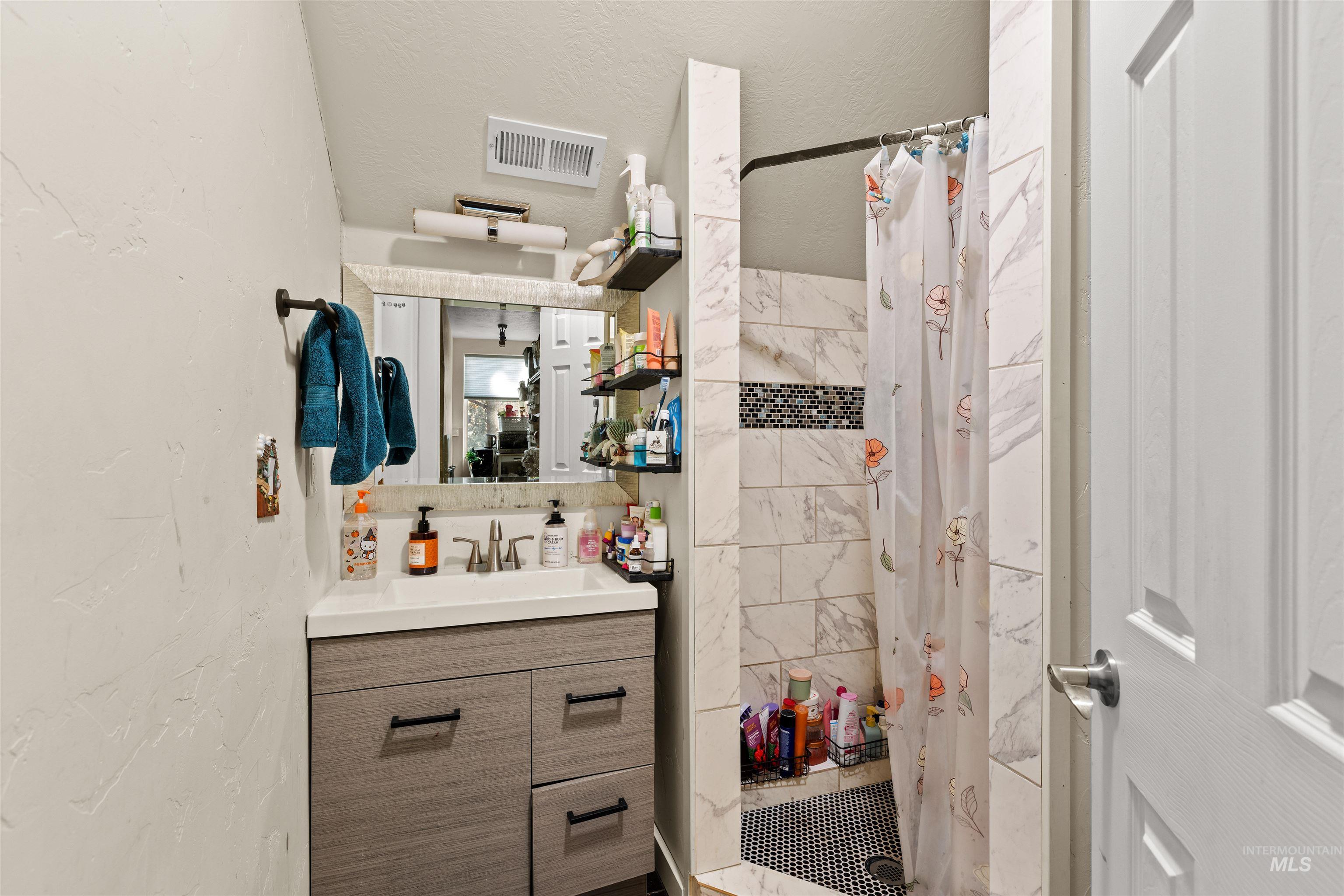 Bathroom featuring vanity, a shower stall, a textured wall, and a textured ceiling