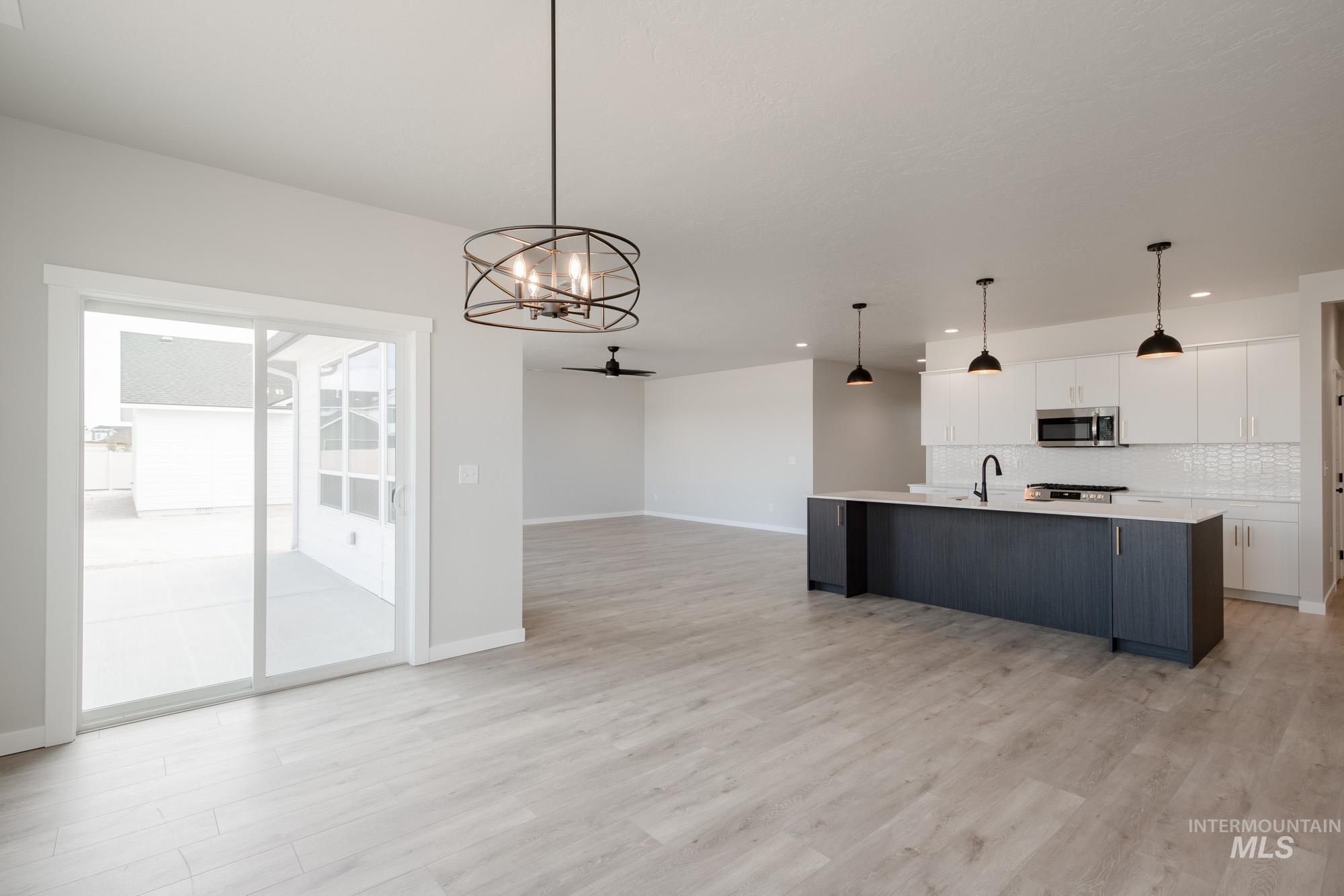 Kitchen featuring white cabinets, an island with sink, a chandelier, hanging light fixtures, and tasteful backsplash