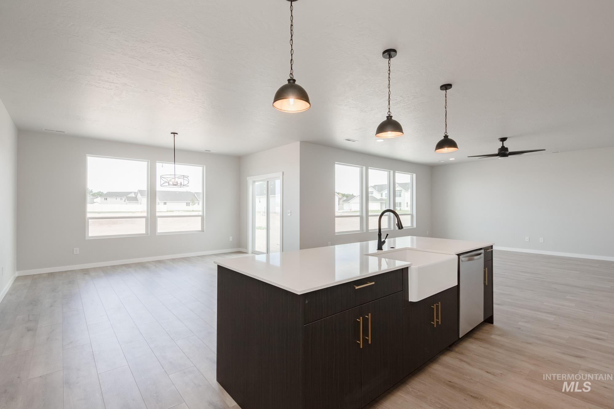 Kitchen featuring open floor plan, decorative light fixtures, ceiling fan, light wood-style flooring, and a textured ceiling