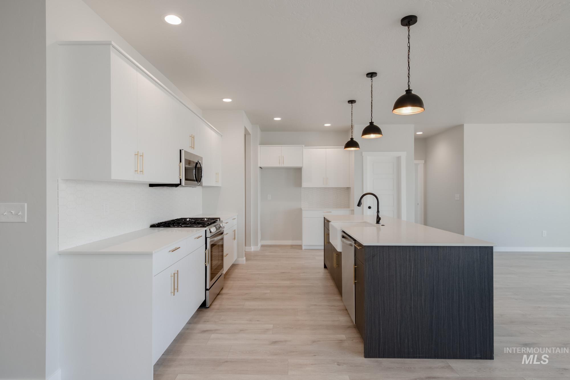 Kitchen with appliances with stainless steel finishes, white cabinetry, light wood-style floors, hanging light fixtures, and tasteful backsplash