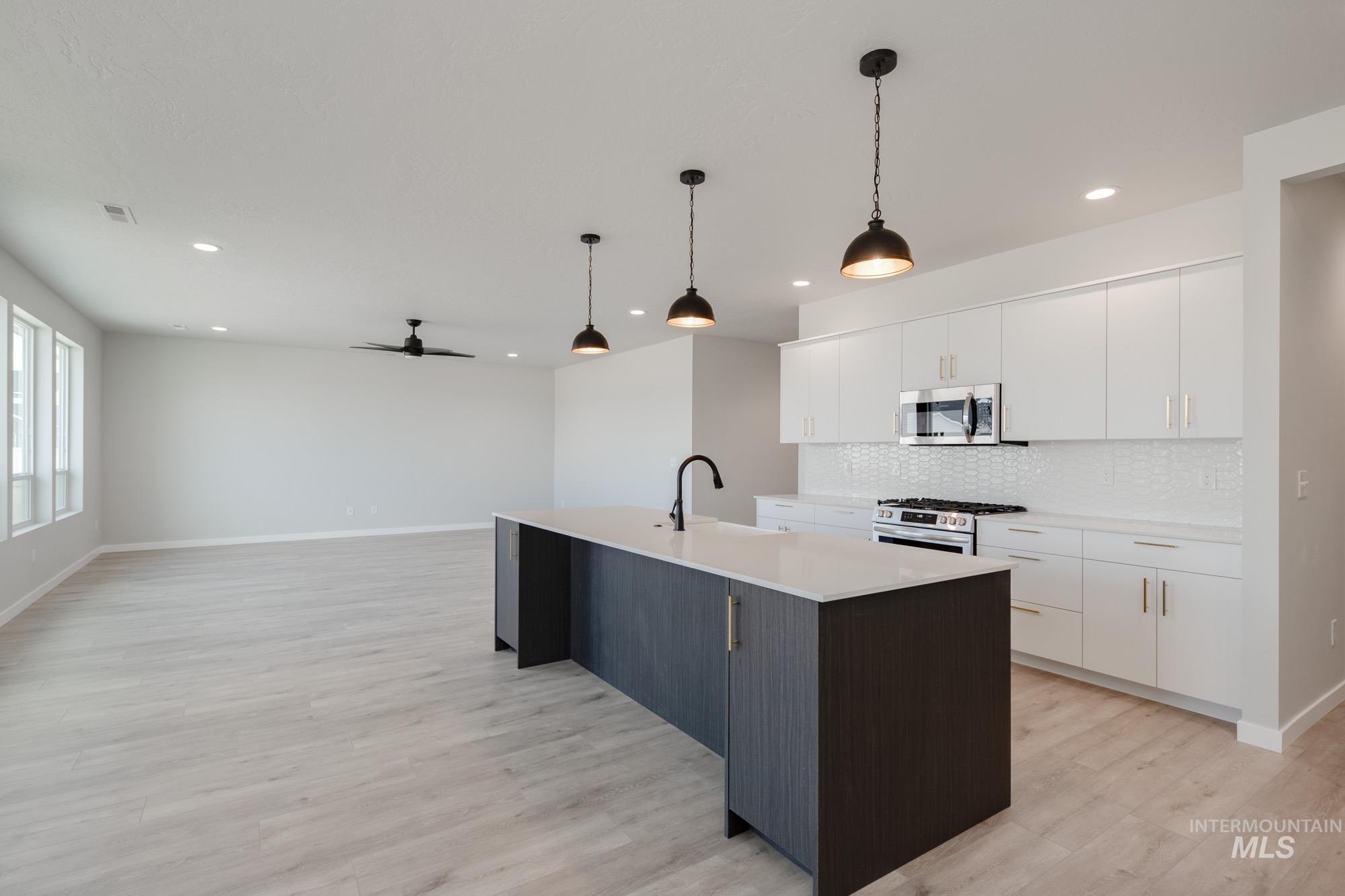 Kitchen featuring white cabinets, ceiling fan, an island with sink, hanging light fixtures, and recessed lighting