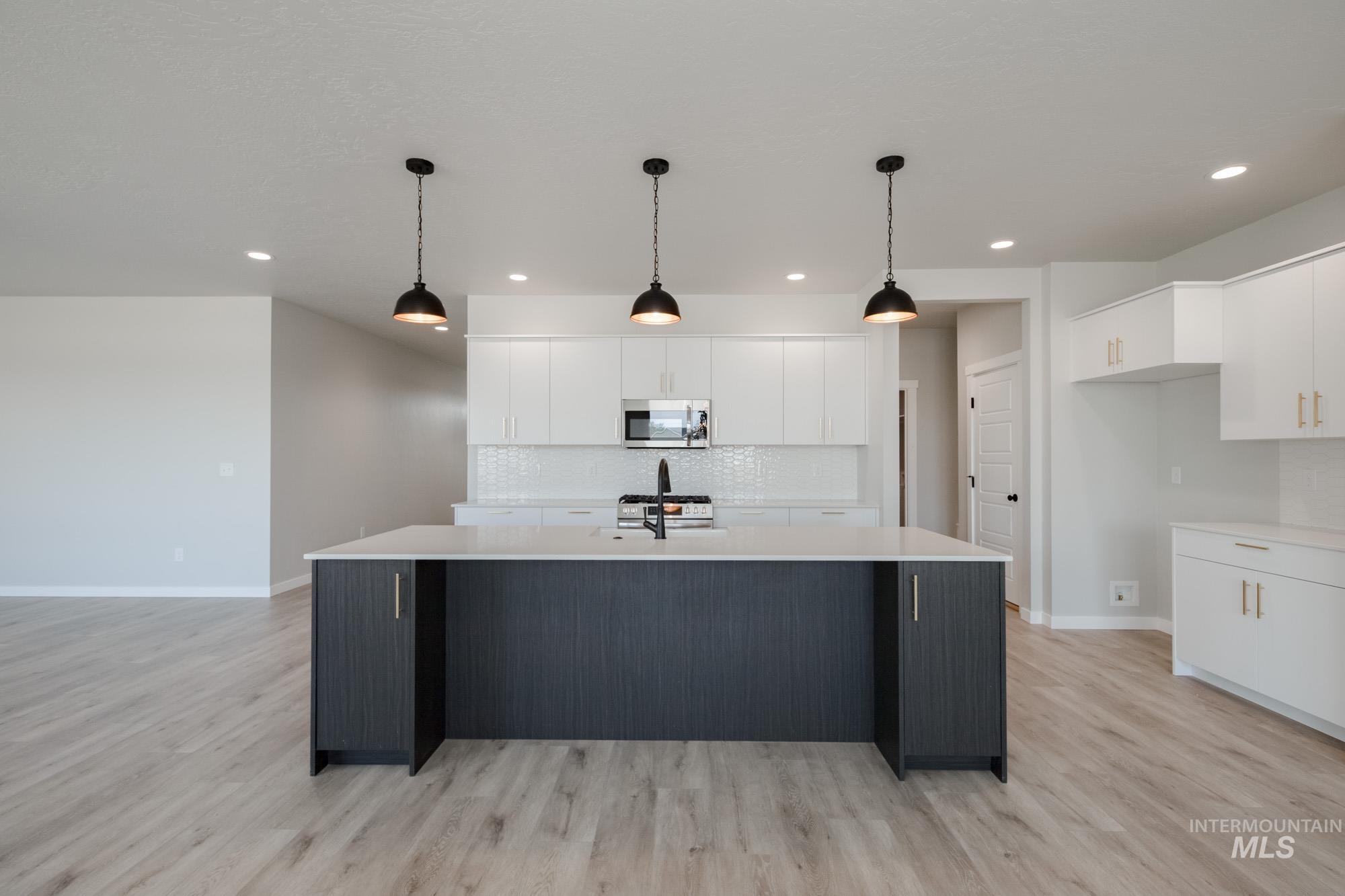 Kitchen featuring decorative backsplash, white cabinets, a center island with sink, pendant lighting, and light wood-type flooring