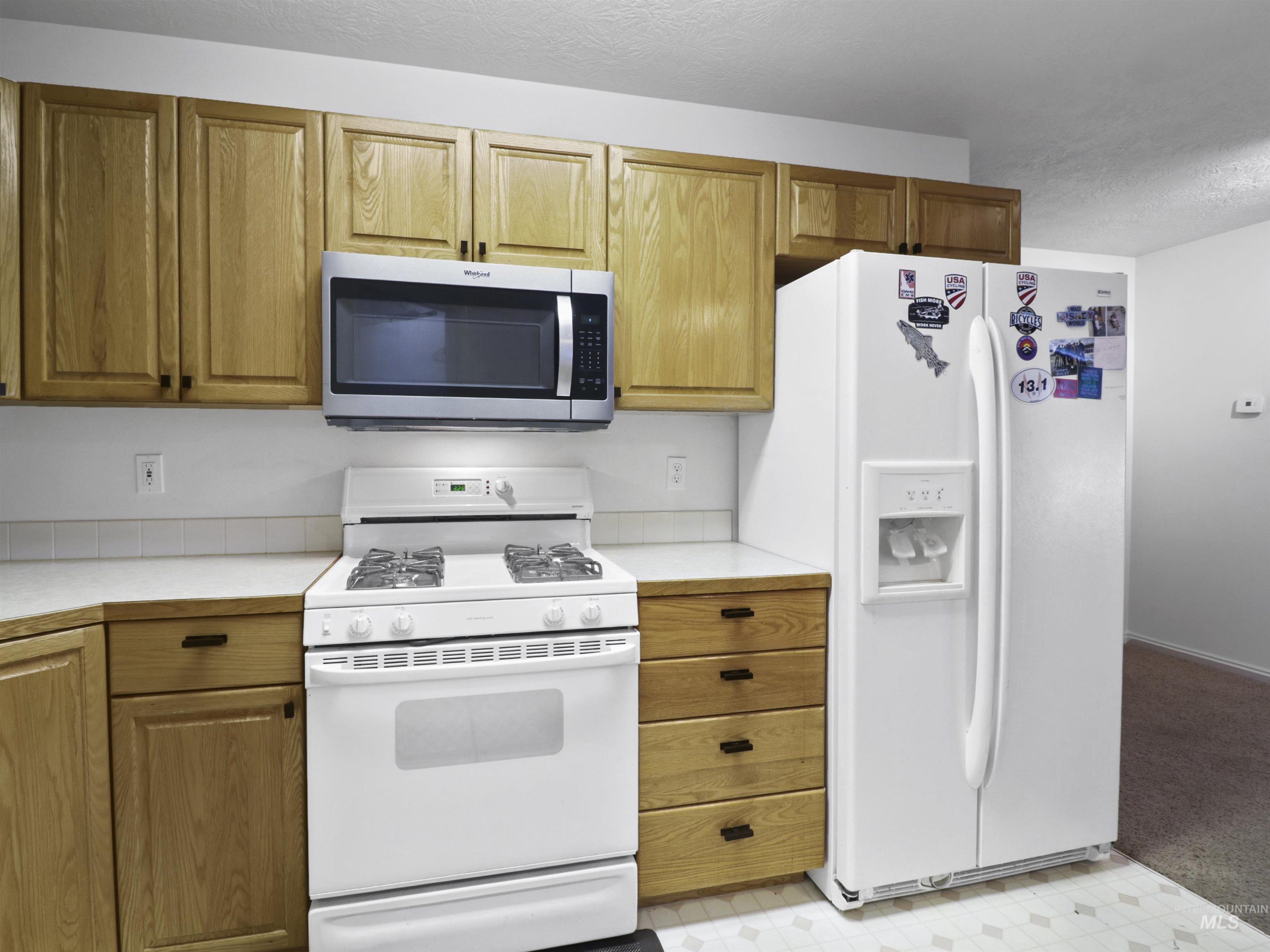 Kitchen featuring white appliances, light countertops, brown cabinetry, and a textured ceiling