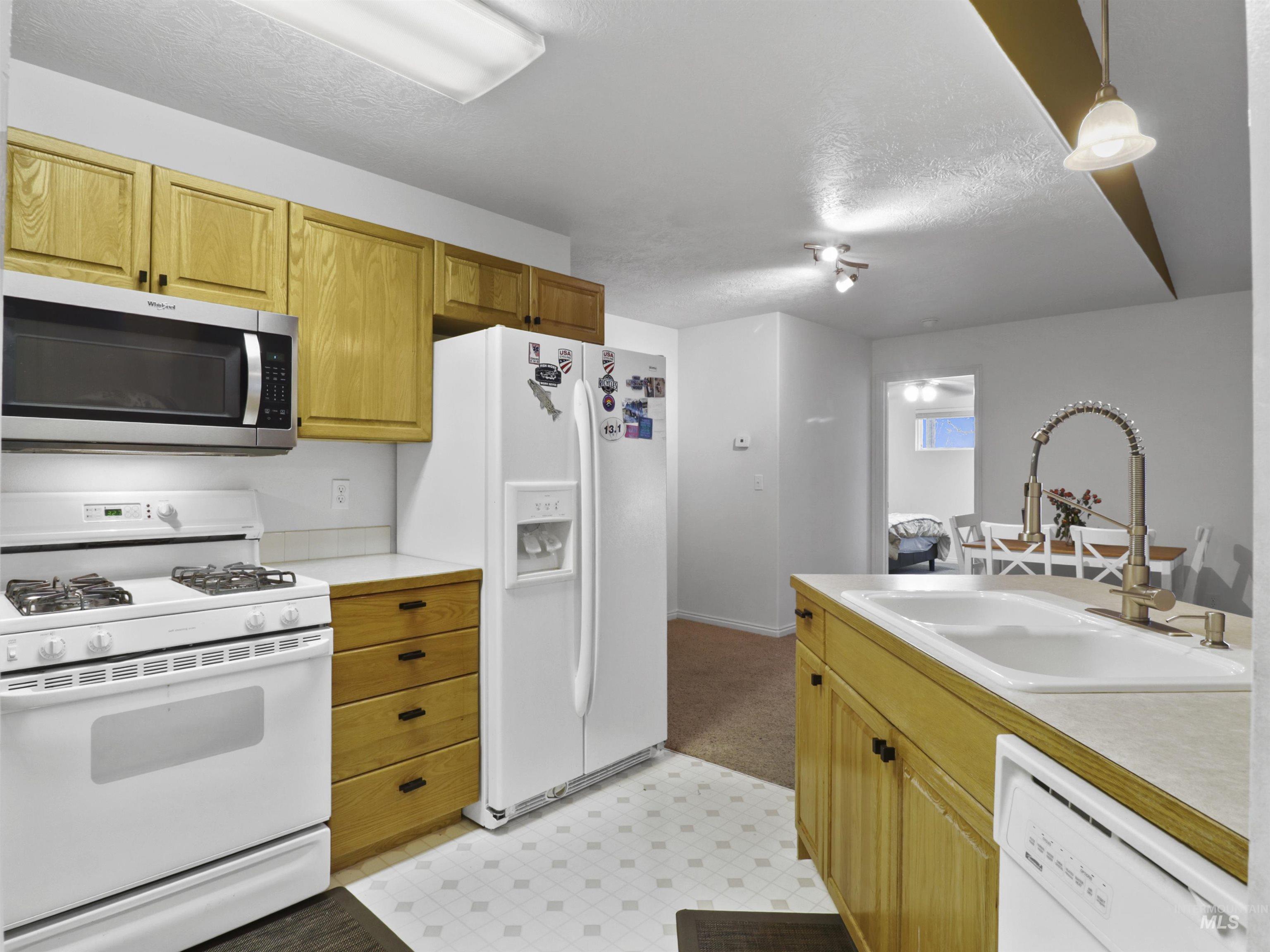 Kitchen with white appliances, light flooring, light countertops, decorative light fixtures, and a textured ceiling