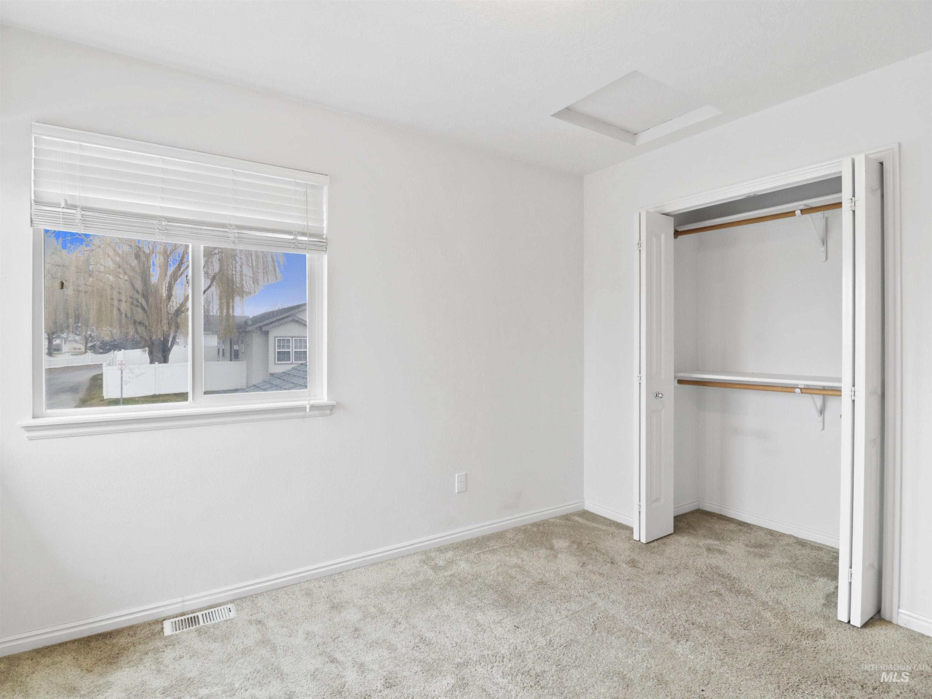 Unfurnished bedroom with attic access, light carpet, and a closet