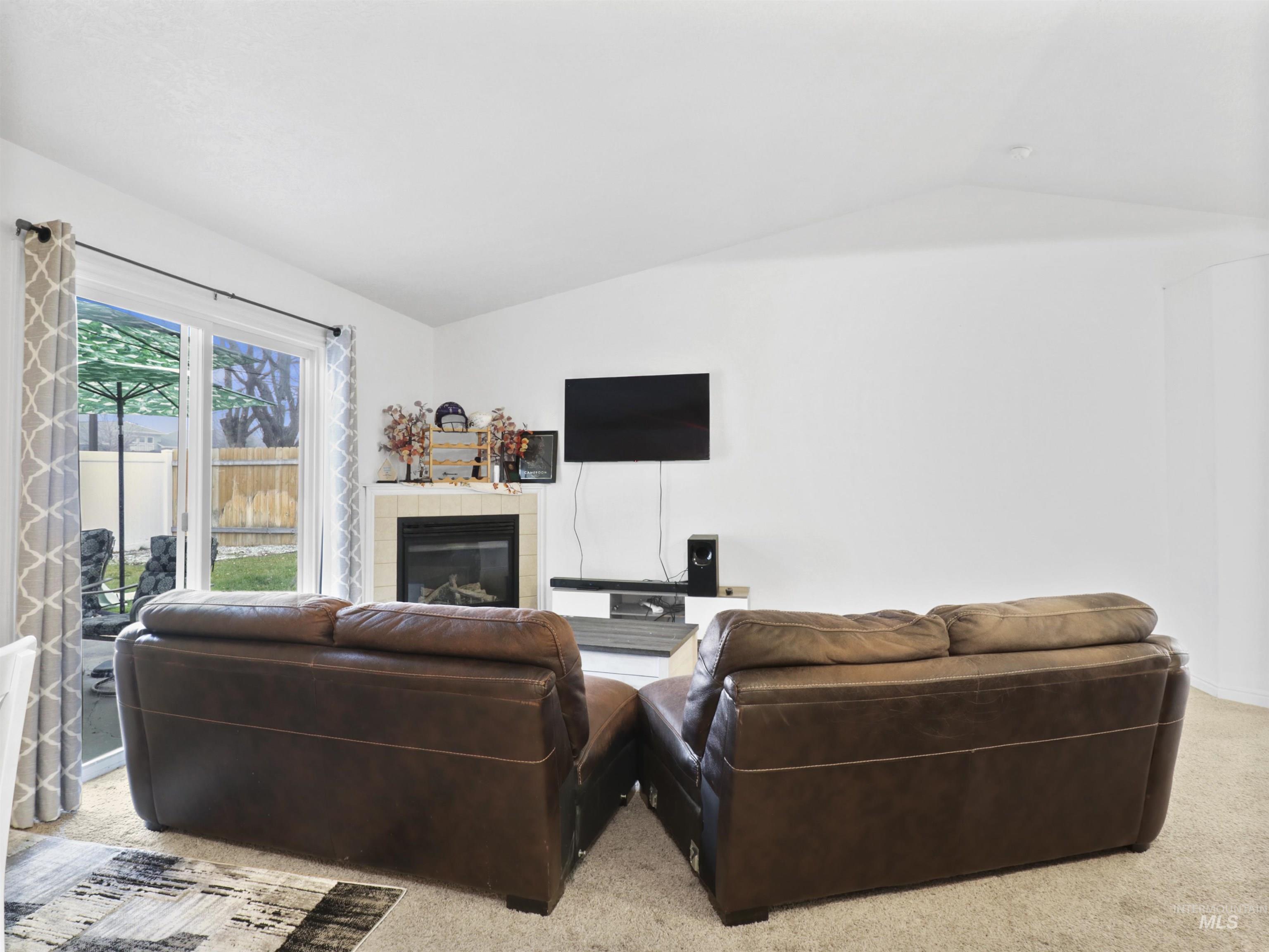 Living room with light colored carpet, a fireplace, and lofted ceiling
