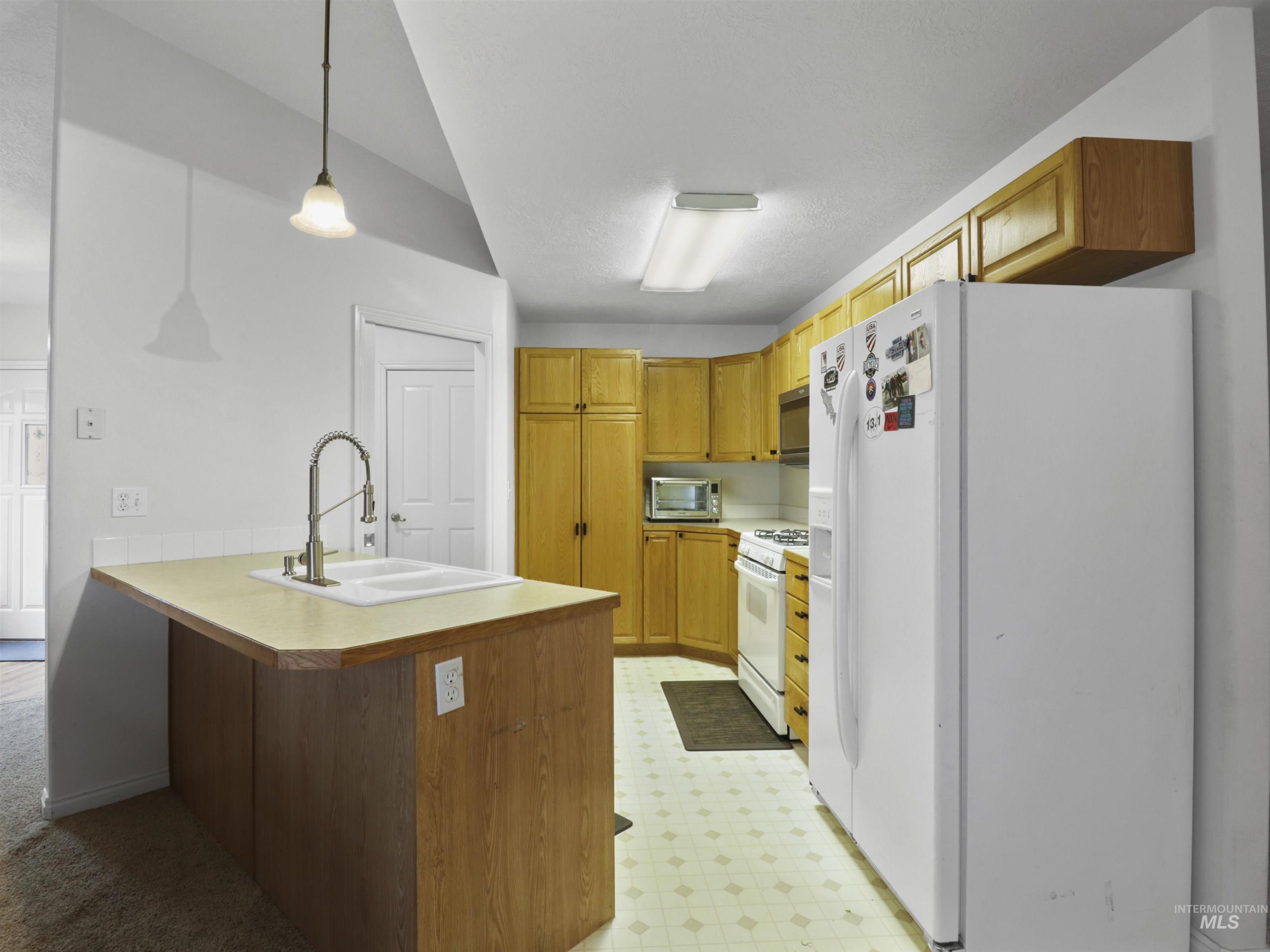 Kitchen featuring white appliances, light floors, decorative light fixtures, and light countertops