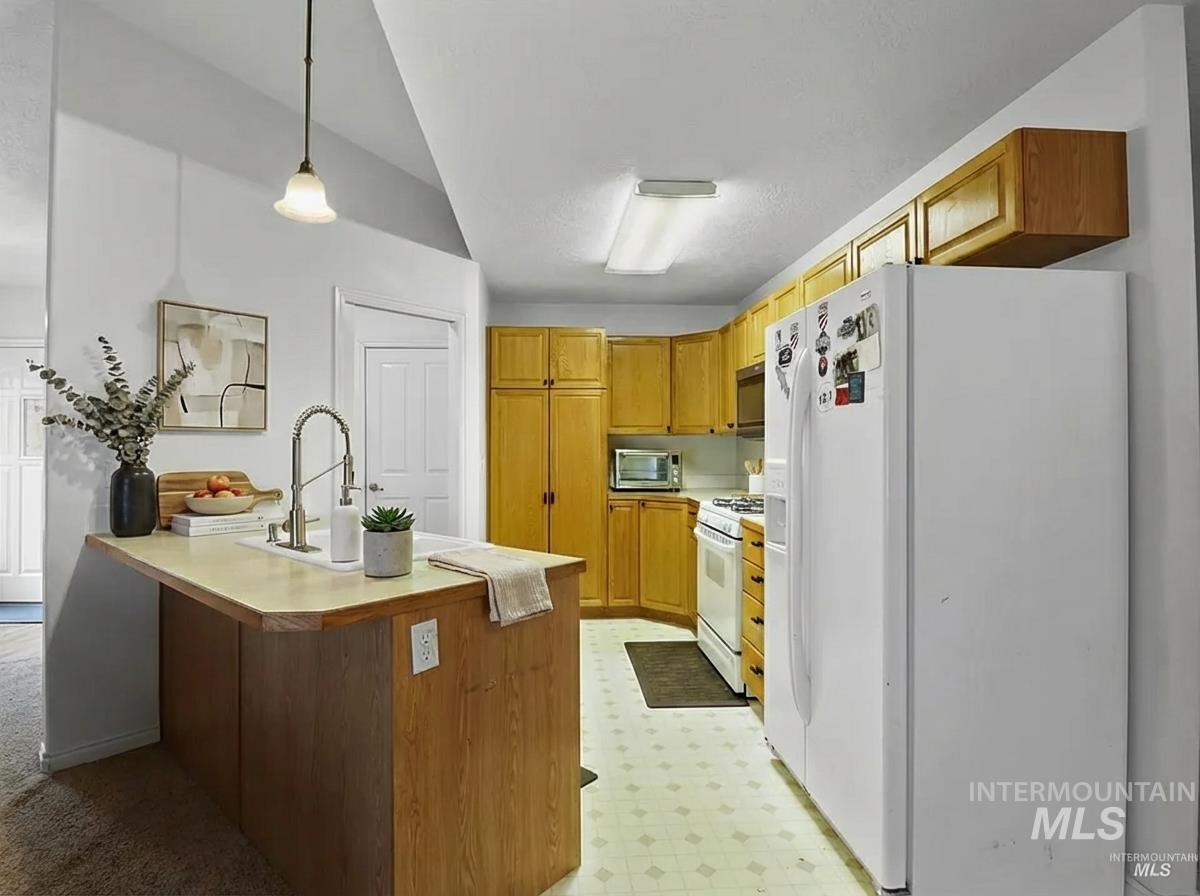 Kitchen featuring light countertops, white appliances, a peninsula, light floors, and decorative light fixtures