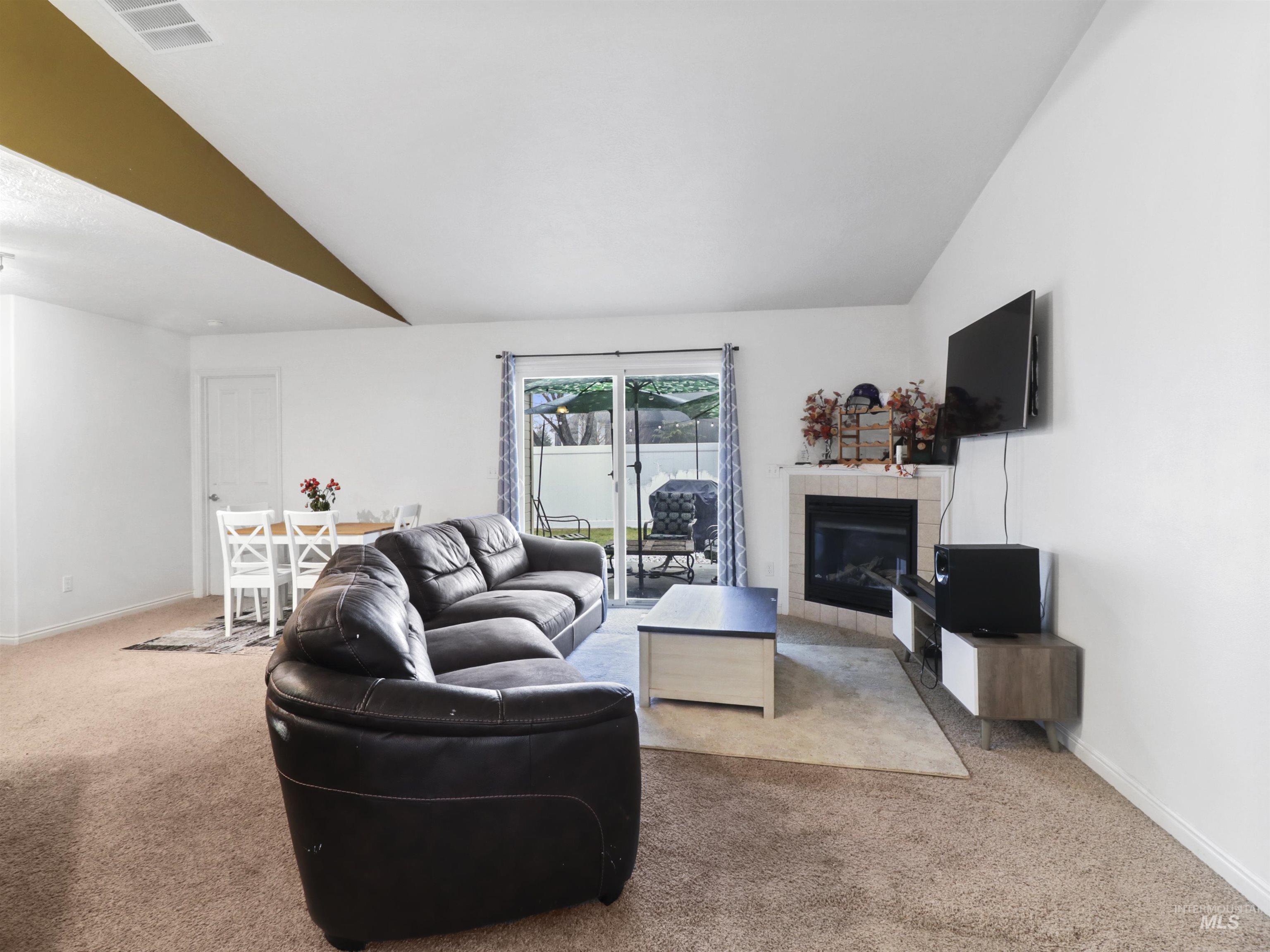 Living area with lofted ceiling, a tile fireplace, and light carpet