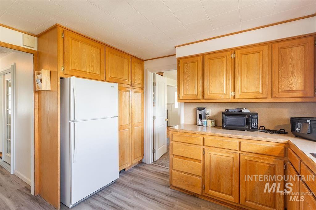 Kitchen with freestanding refrigerator, black microwave, light wood-type flooring, and light countertops