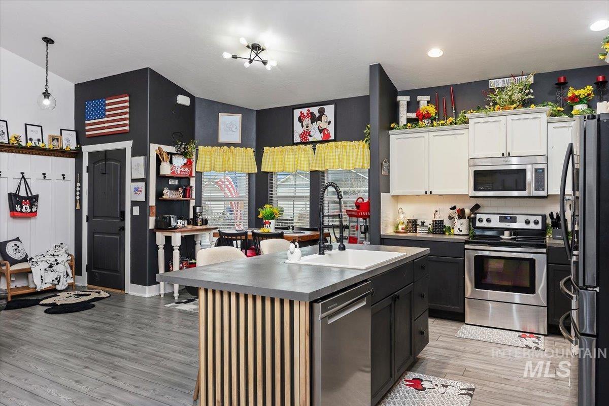 Kitchen with stainless steel appliances, light wood-style floors, a kitchen island with sink, two tone cabinetry, and tasteful backsplash