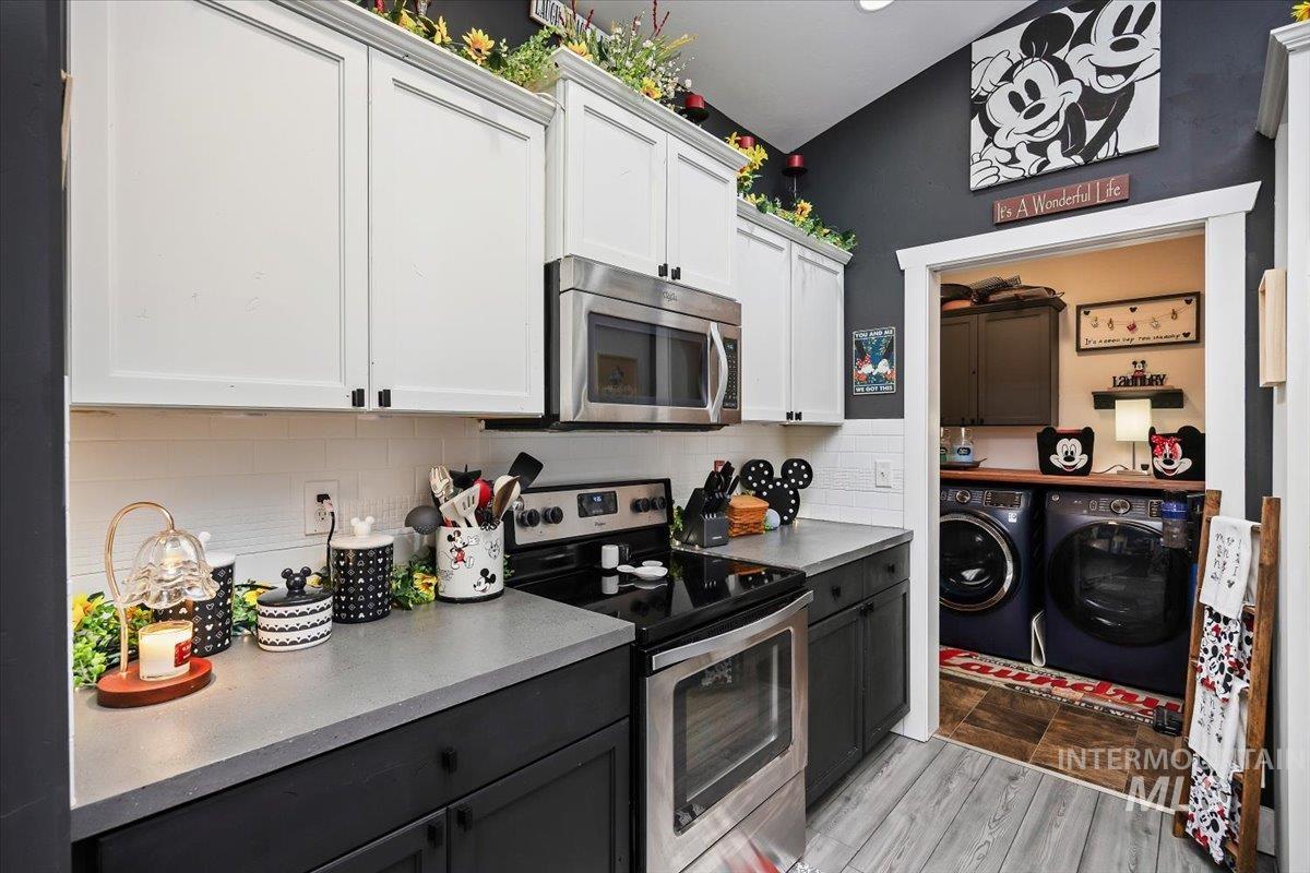 Two tone kitchen with stainless steel appliances, two tone cabinets, separate washer and dryer, light wood-style flooring, and tasteful backsplash