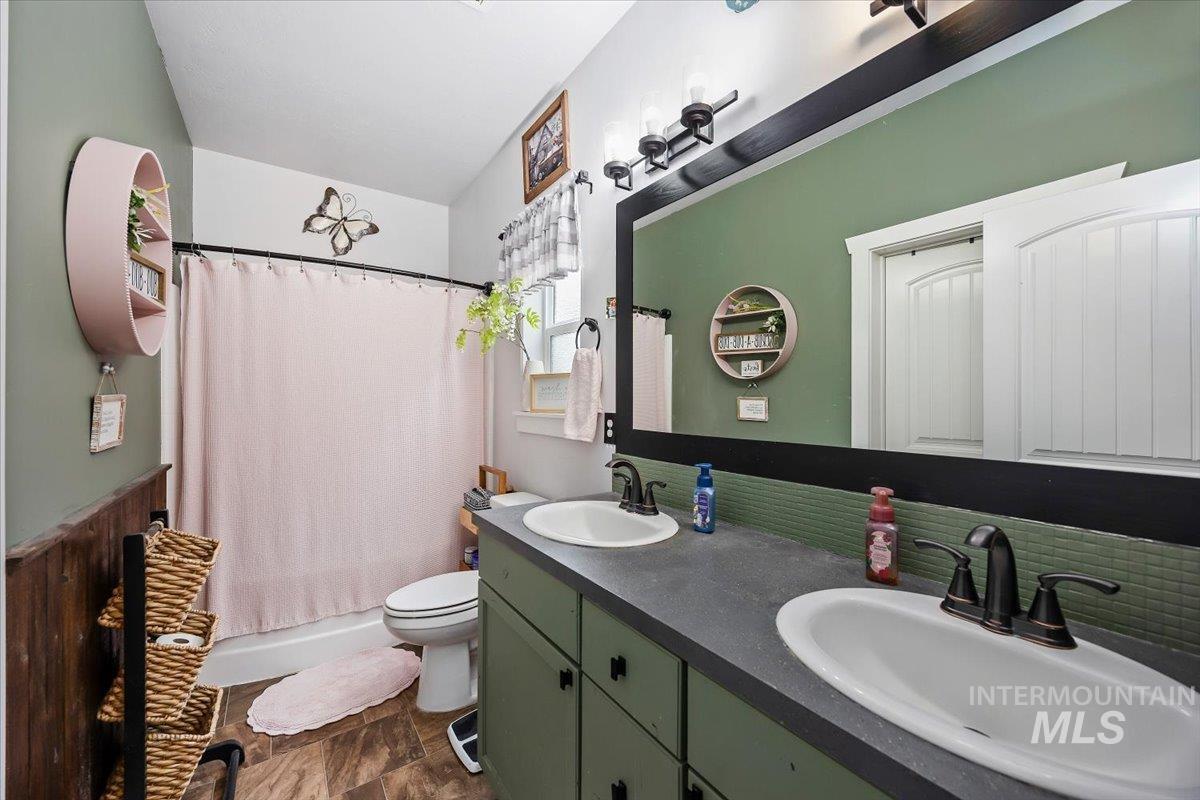 Full bath featuring double vanity, shower / bath combo with shower curtain, and a wainscoted wall