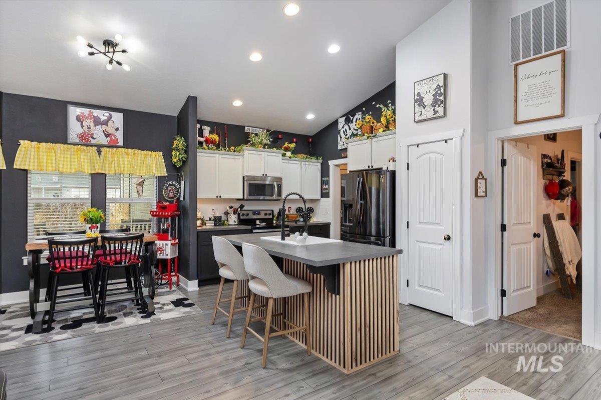 Kitchen featuring a kitchen breakfast bar, white cabinetry, an island with sink, dark countertops, and stainless steel appliances