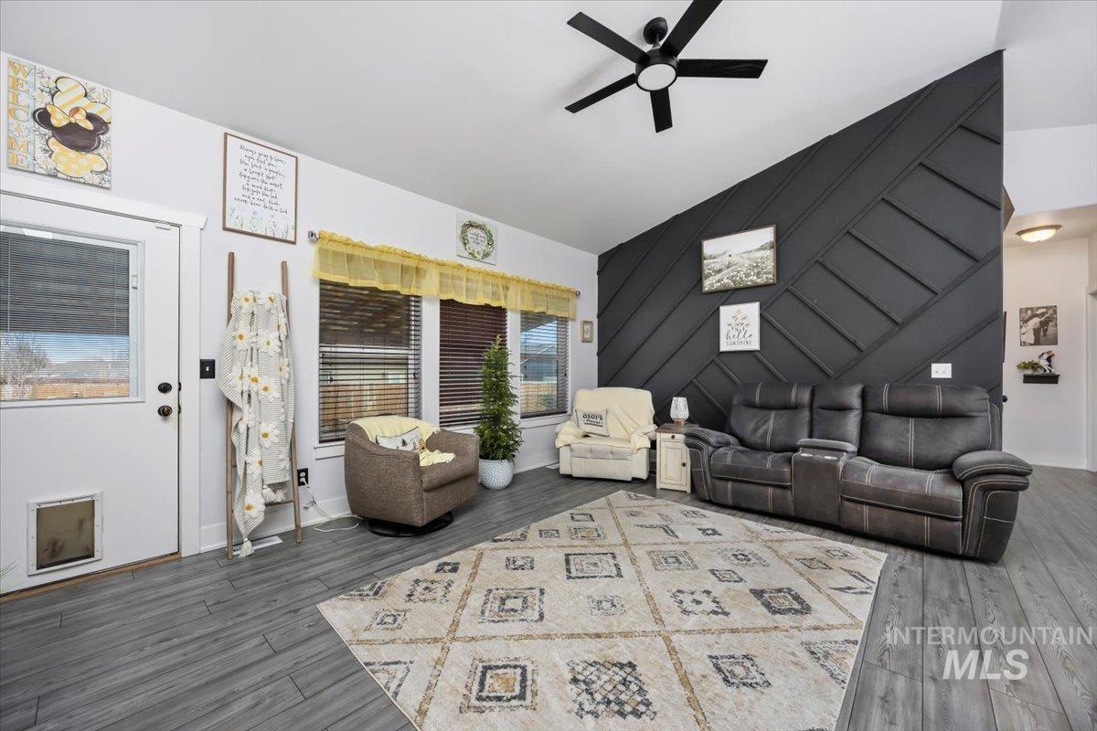 Living area with a decorative wall, ceiling fan, an accent wall, dark wood-style flooring, and lofted ceiling