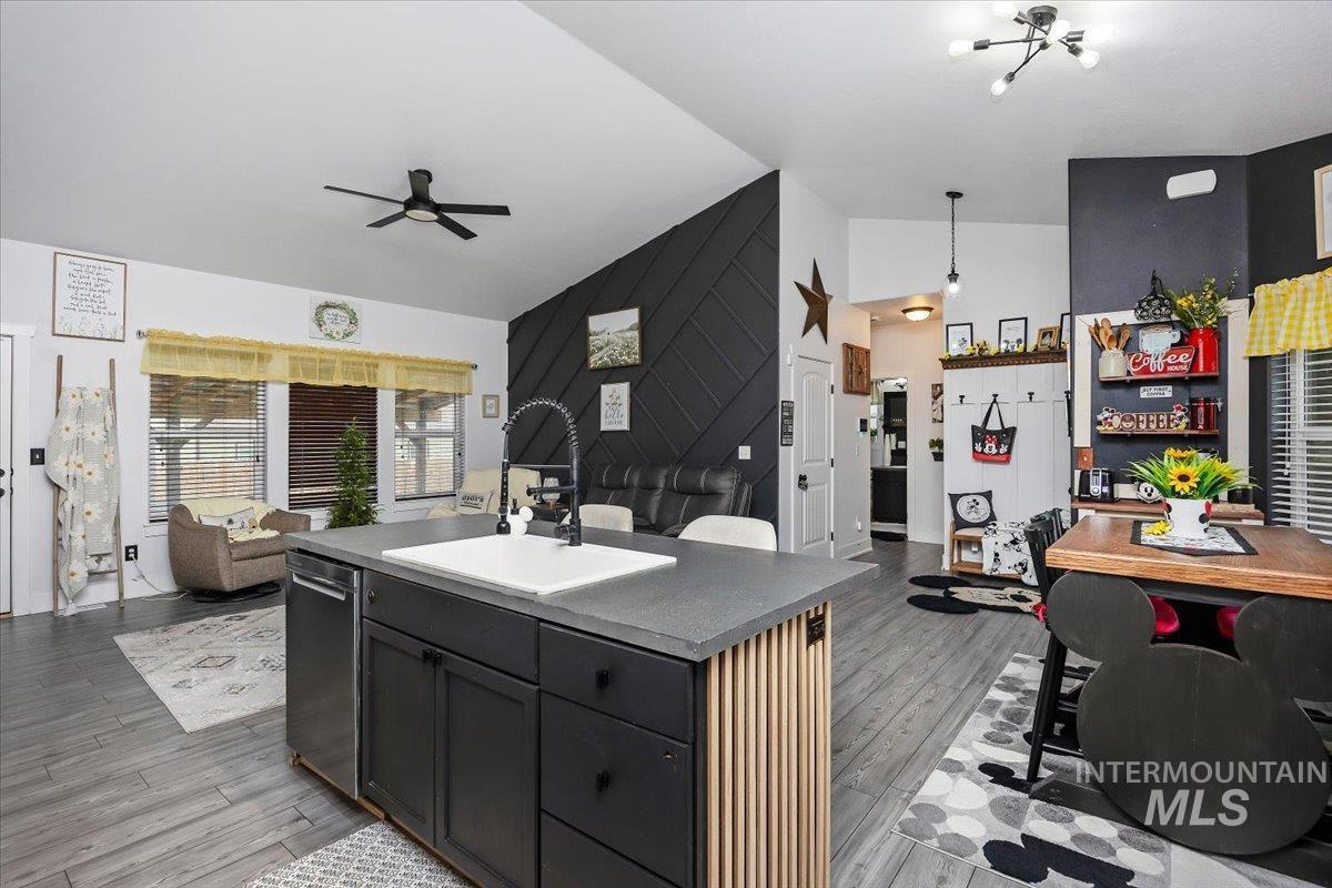 Kitchen with lofted ceiling, a center island with sink, open floor plan, ceiling fan, and wood finished floors