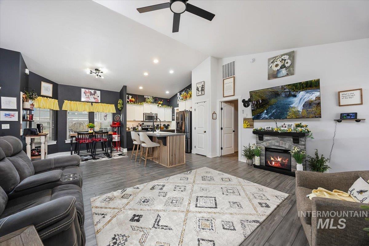 Living room featuring a ceiling fan, dark wood finished floors, a stone fireplace, lofted ceiling, and recessed lighting