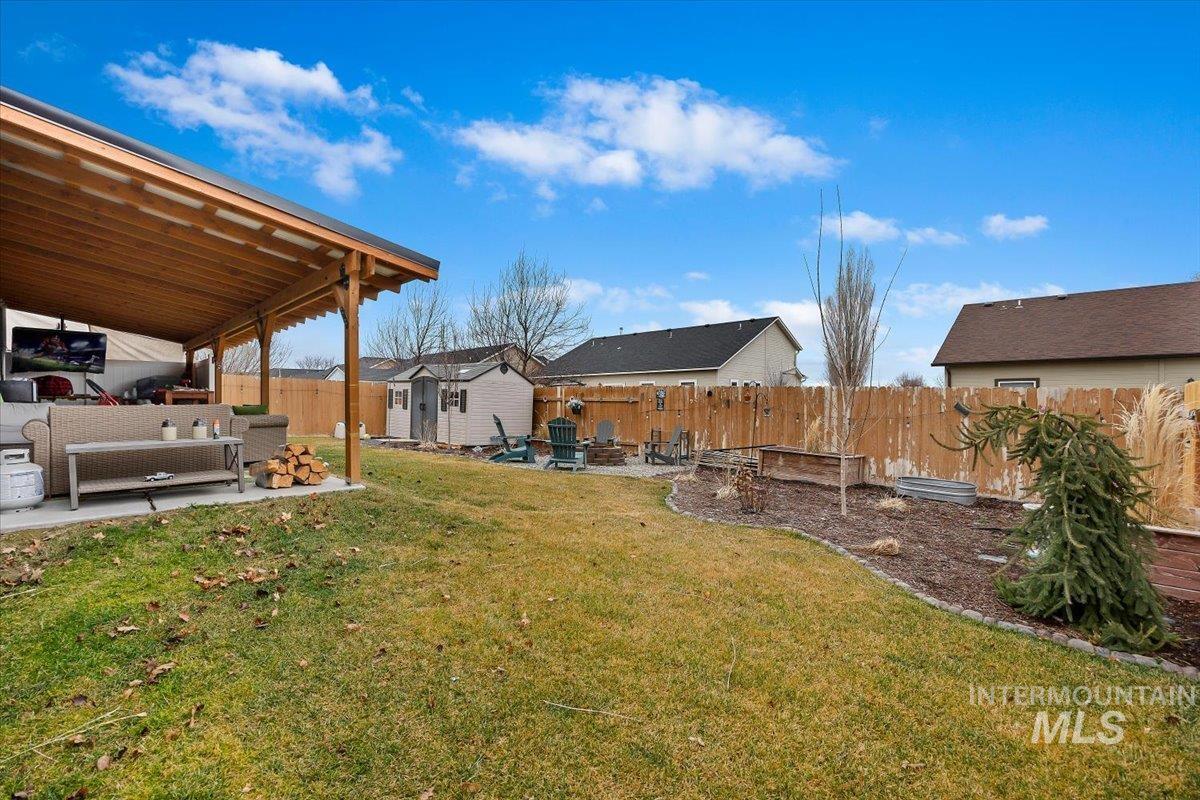 Fenced backyard with a patio area, an outdoor living space with a fire pit, and a storage unit