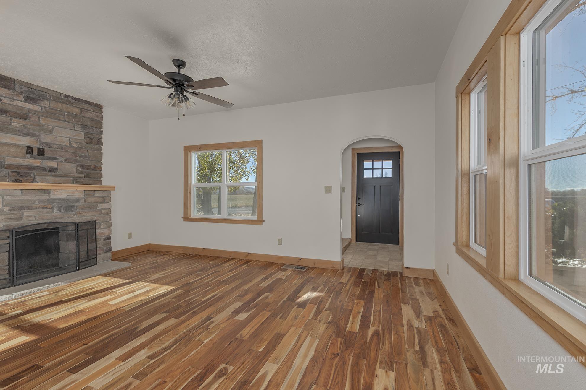 Unfurnished living room featuring a fireplace, wood finished floors, plenty of natural light, and a ceiling fan